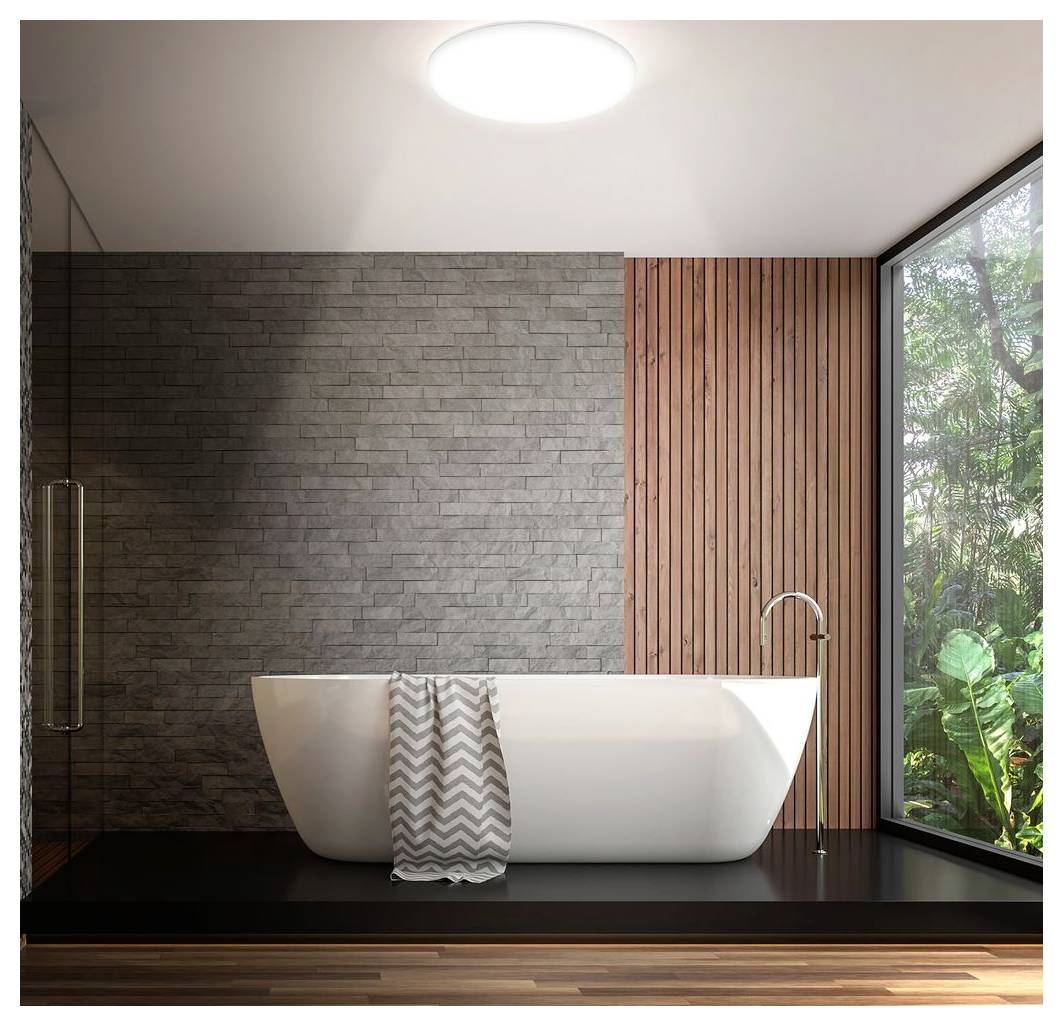 Modernes Badezimmer mit freistehender weißer Badewanne auf einer erhöhten dunklen Plattform, grauen Ziegeln und Holzlattenwänden sowie einem großen Fenster mit Ausblick auf Grünflächen.