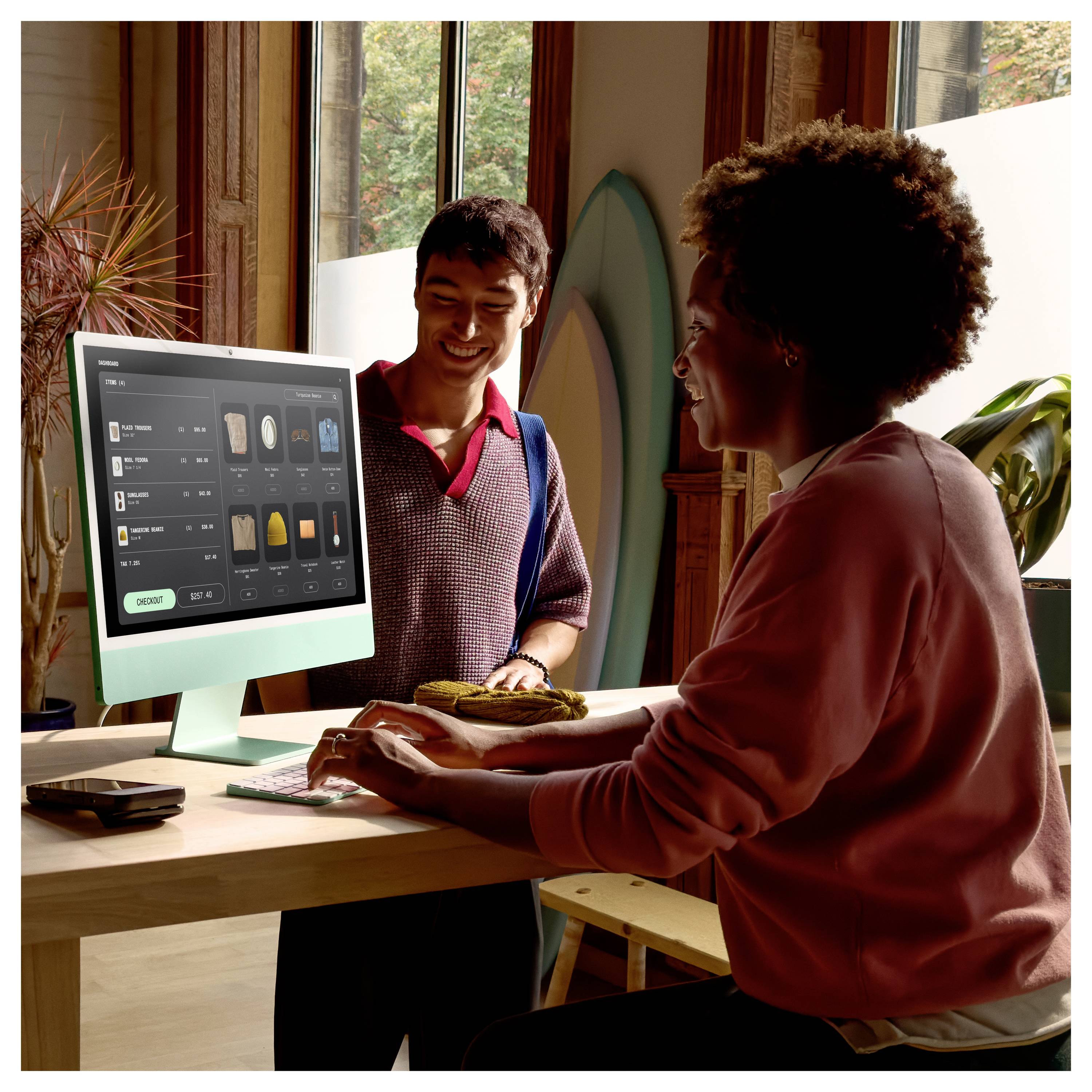 Zwei Personen in einem hellen Geschäft nutzen einen Desktop-Computer, der eine Produktbestelloberfläche anzeigt, während sie an einem Tresen Artikel besprechen.