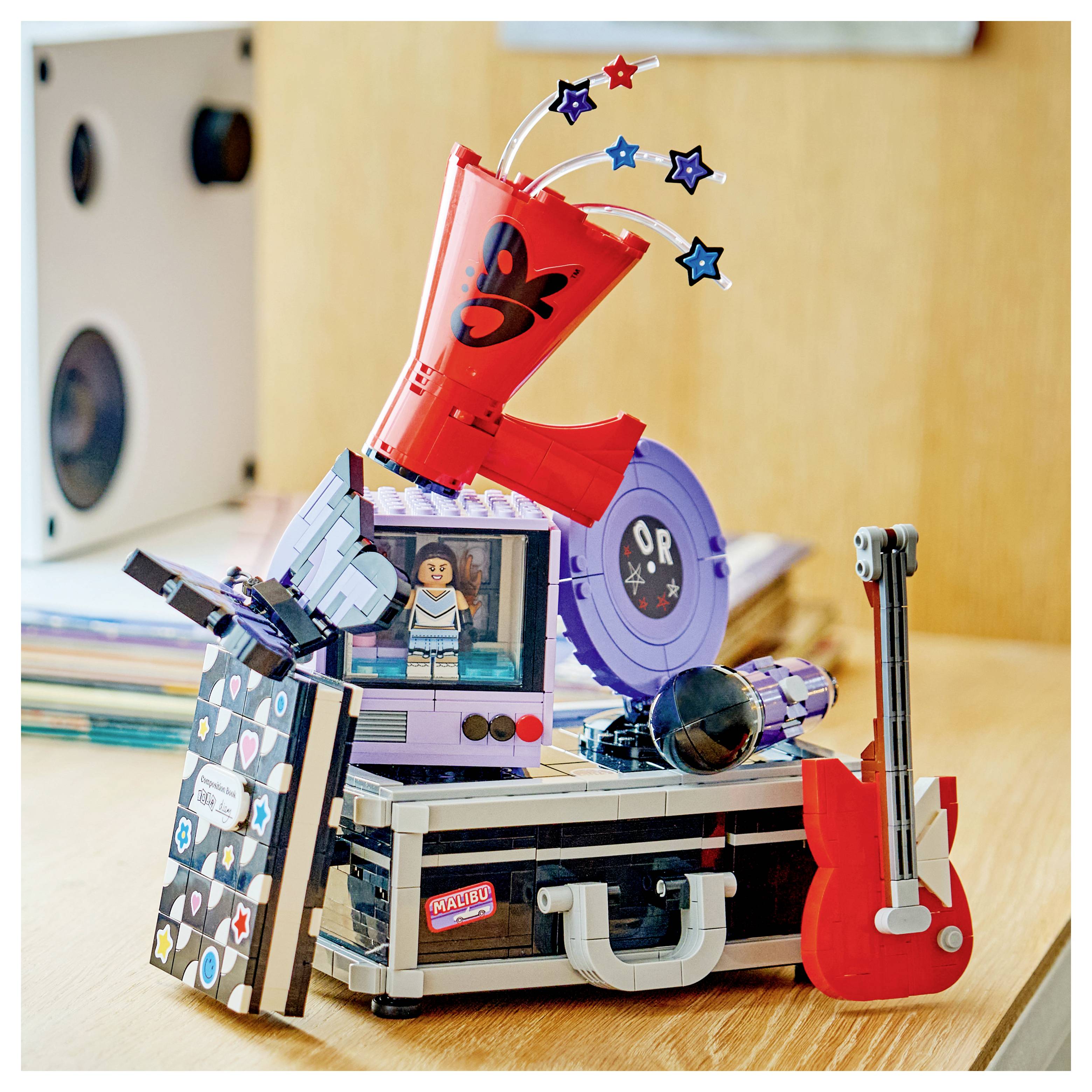 Eine bunte LEGO-ähnliche Musikbühnen-Ausstellung mit einer Minifigur, rotem Horn, Plattenspieler, Lautsprechern und einer roten Gitarre auf einer kofferähnlichen Basis.