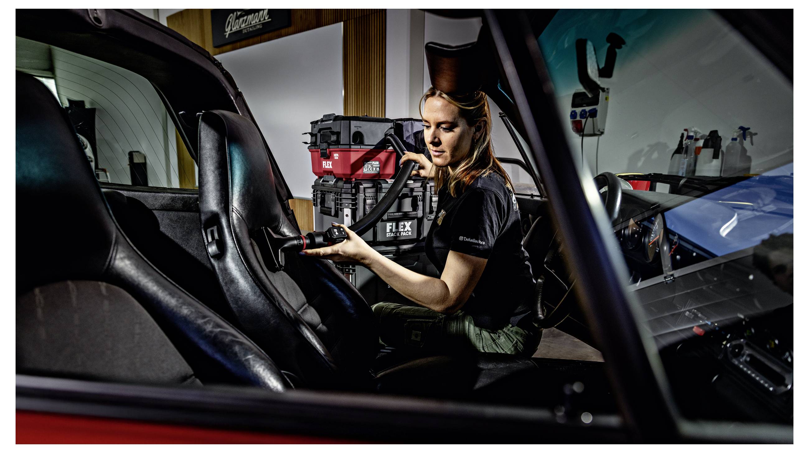 Eine Frau bedient ein rotes und schwarzes FLEX-Elektrowerkzeug in einer Fahrzeugwerkstatt, sitzt im Fahrzeuginnenraum und repariert oder wartet Ausrüstungen.