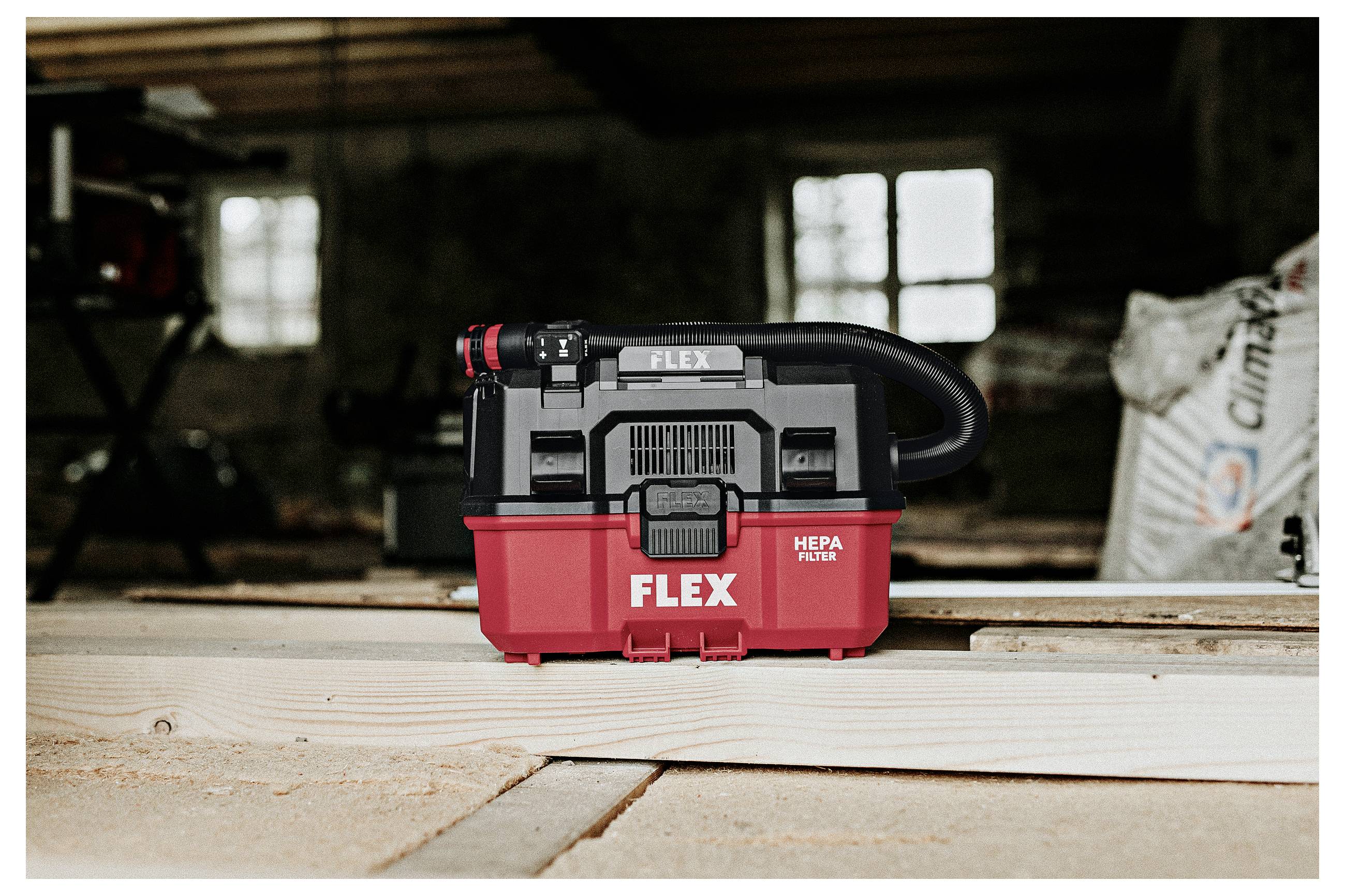 Roter und schwarzer FLEX HEPA-Filter-Staubsauger, der auf Holzdielen in einer dunkel beleuchteten Werkstatt oder Garage steht.