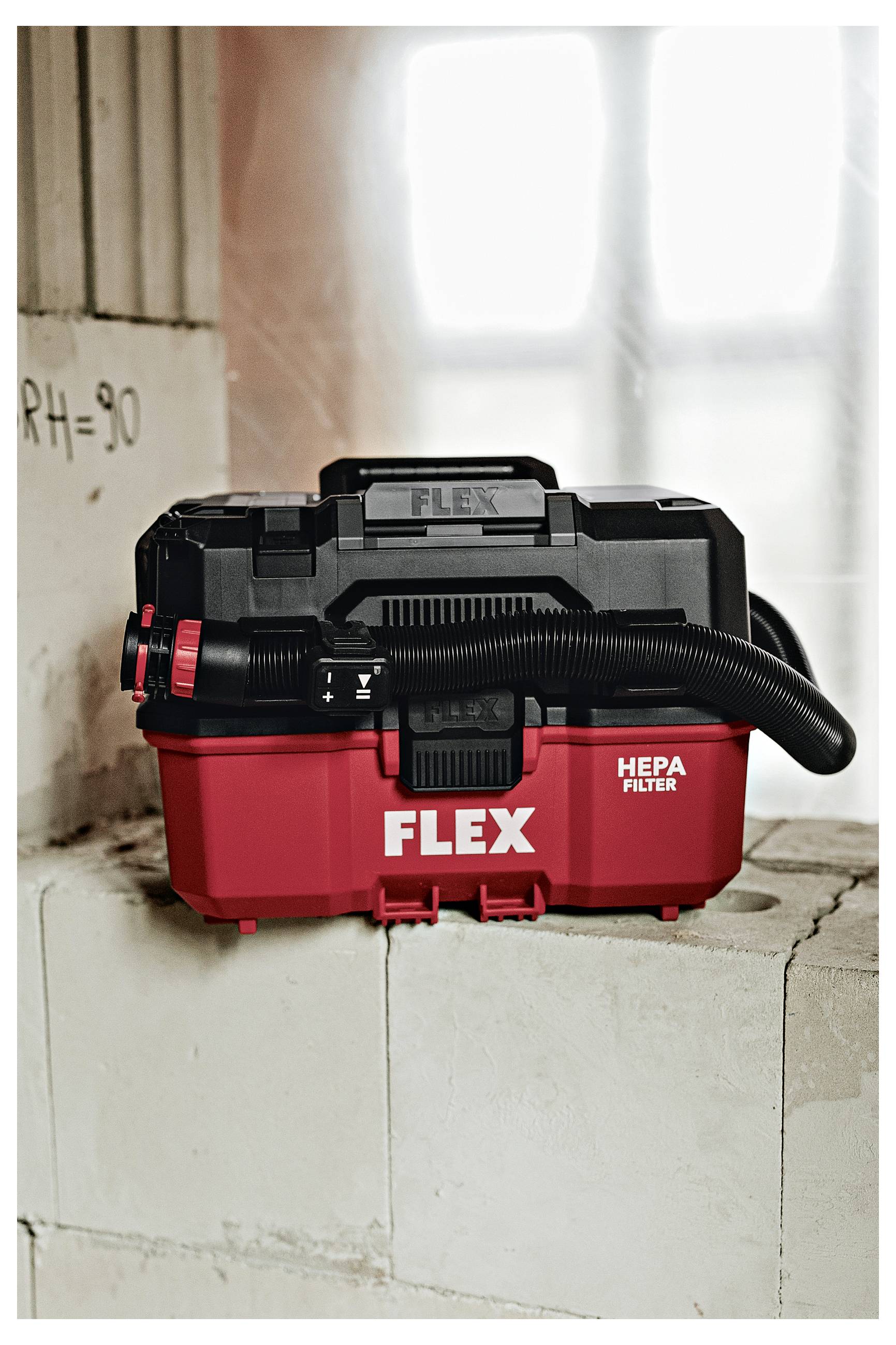 Rot-schwarzer FLEX HEPA-Filter-Staubsauger, gezeigt auf einem Betonblock in einer Werkstatt oder Baustelle.
