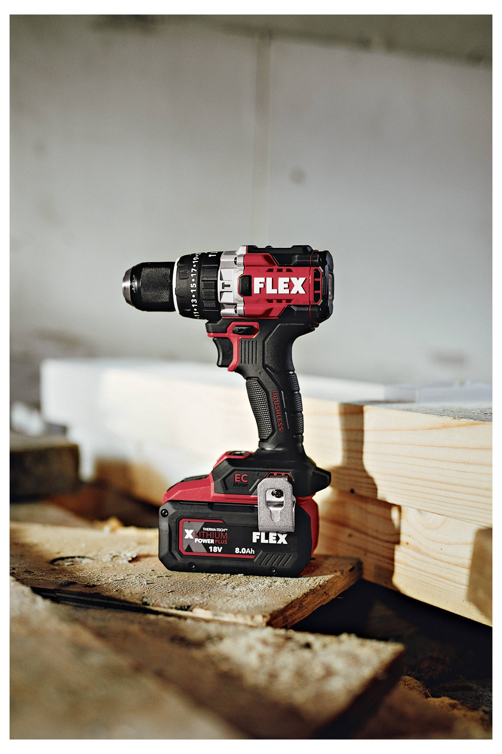 FLEX Akku-Bohrmaschine steht auf einer Werkbank neben gestapeltem Holz in einer Werkstattatmosphäre.