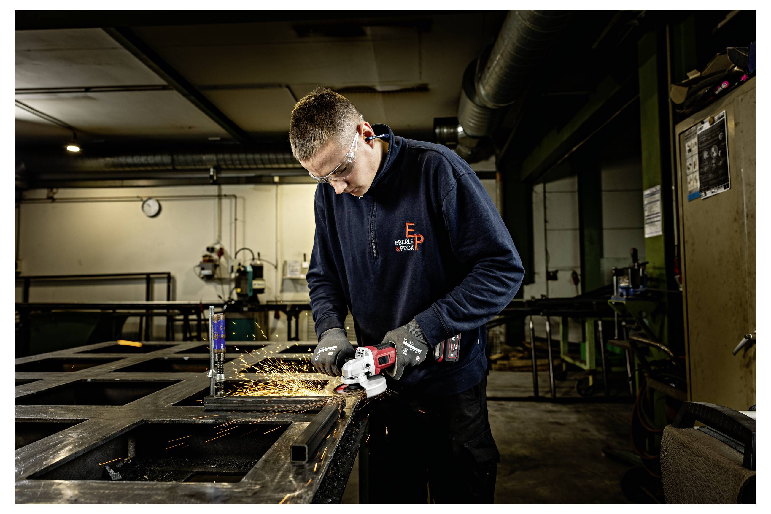 Arbeiter in Schutzausrüstung schleifen Metall in einer Werkstatt und erzeugen Funken beim Schneiden eines Stahlrahmens.