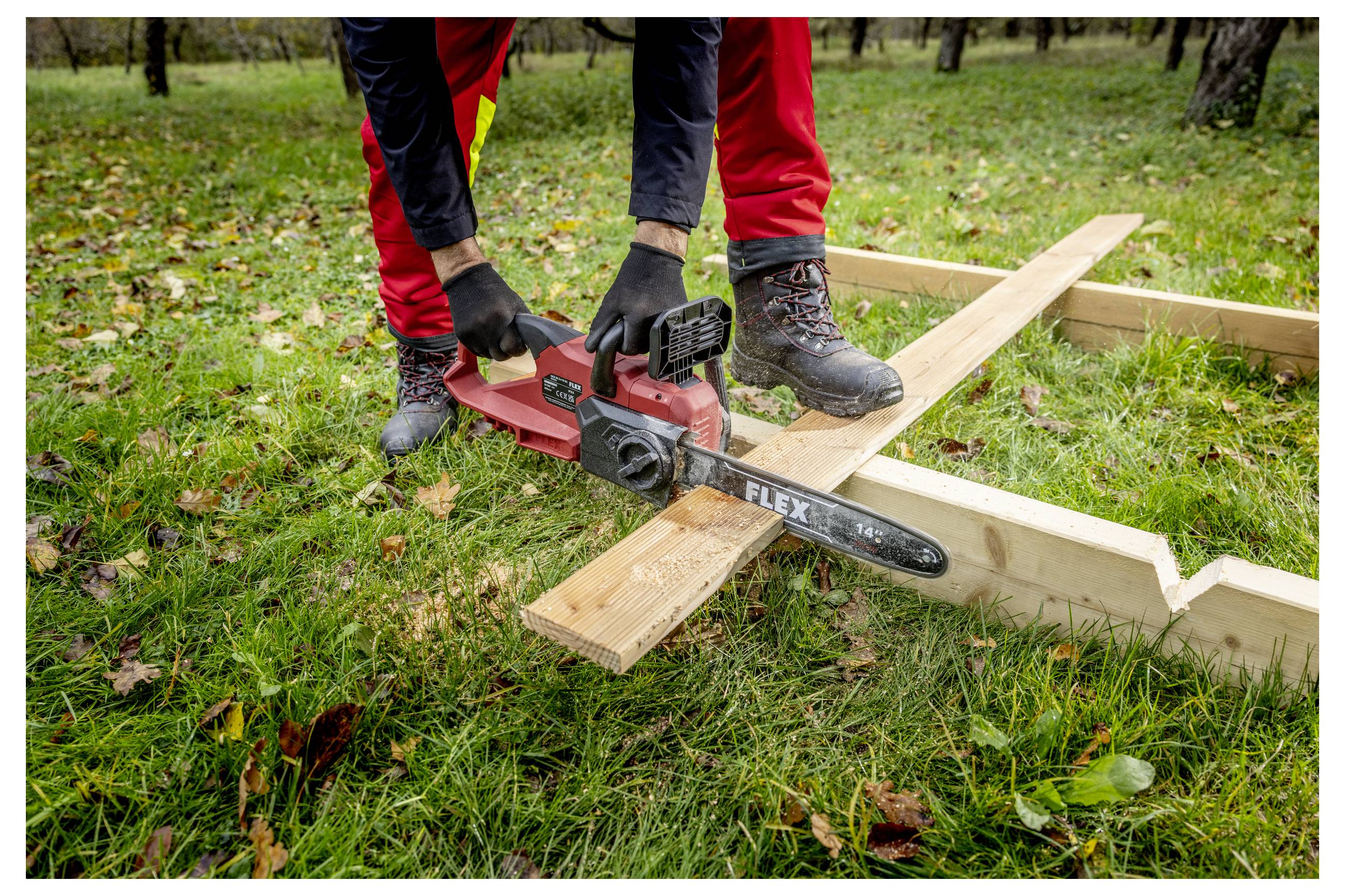 Person mit einer roten Kettensäge, die einen Holzbalken auf Gras schneidet, während sie draußen einen Rahmen baut.