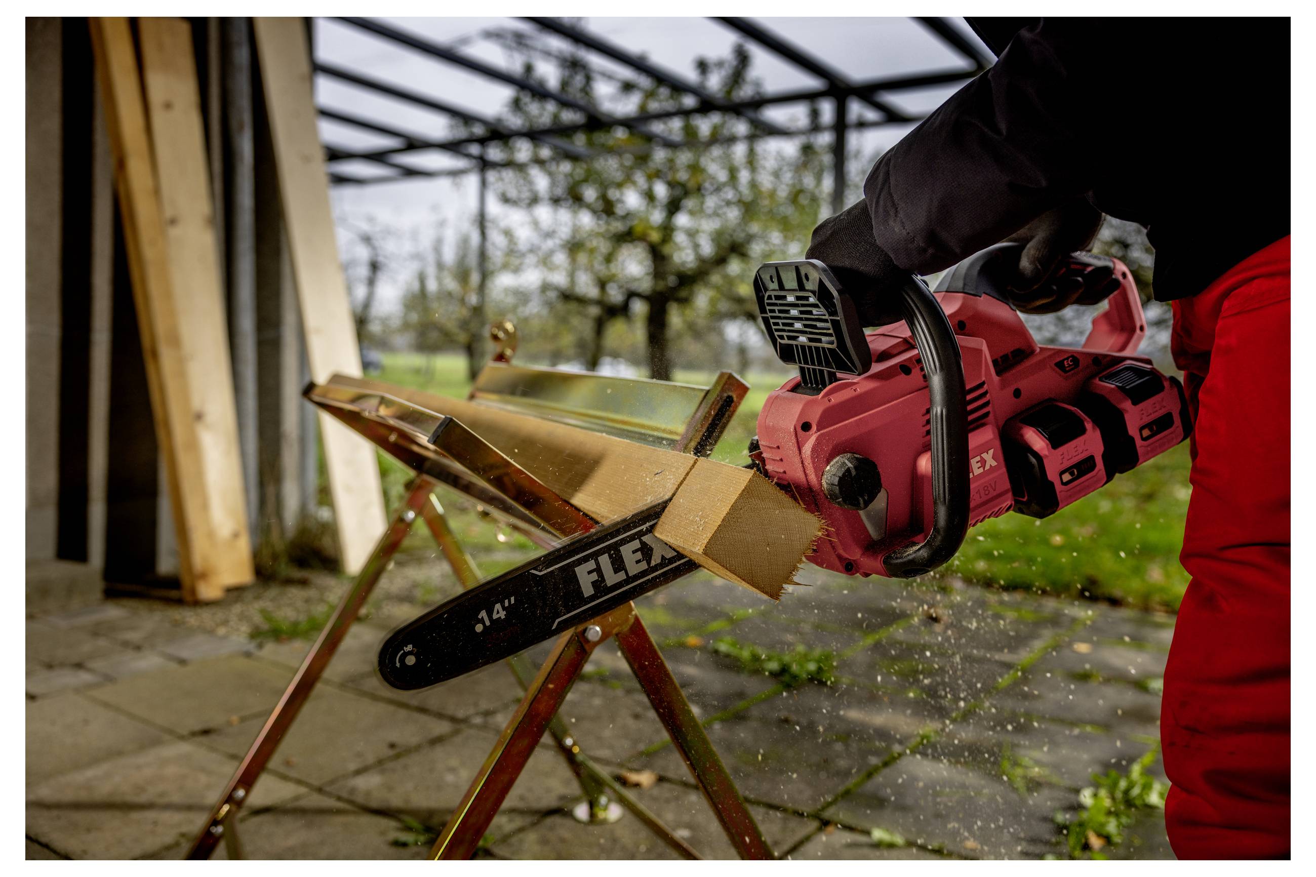 Eine Person benutzt eine rote Kettensäge, um ein Brett zu durchschneiden, das auf einem Sägebock eingespannt ist, in einem Außenarbeitsbereich.