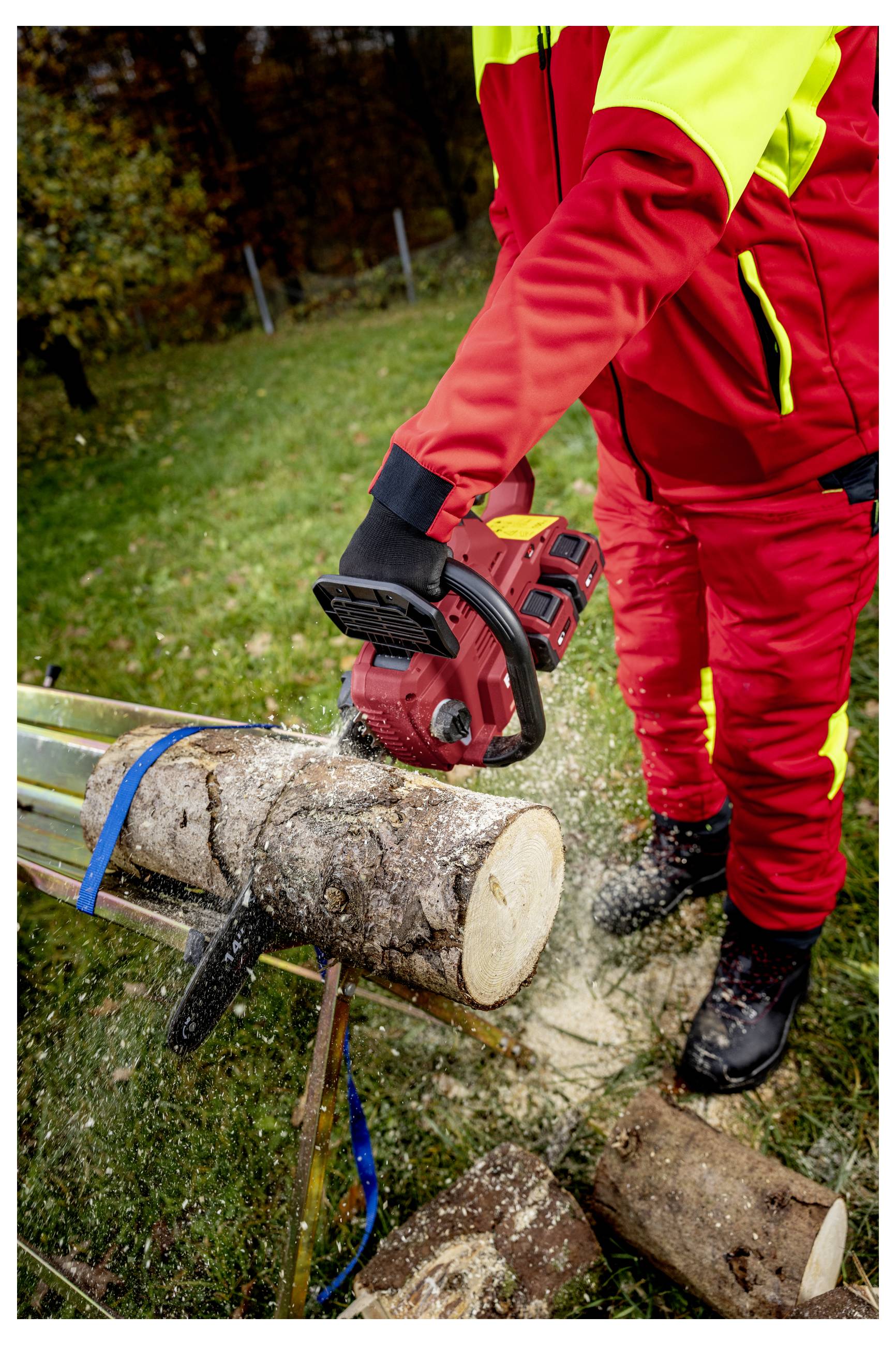 Arbeiter in roter Schutzausrüstung, der mit einer Kettensäge einen Baumstamm auf einem Gestell im Freien schneidet.