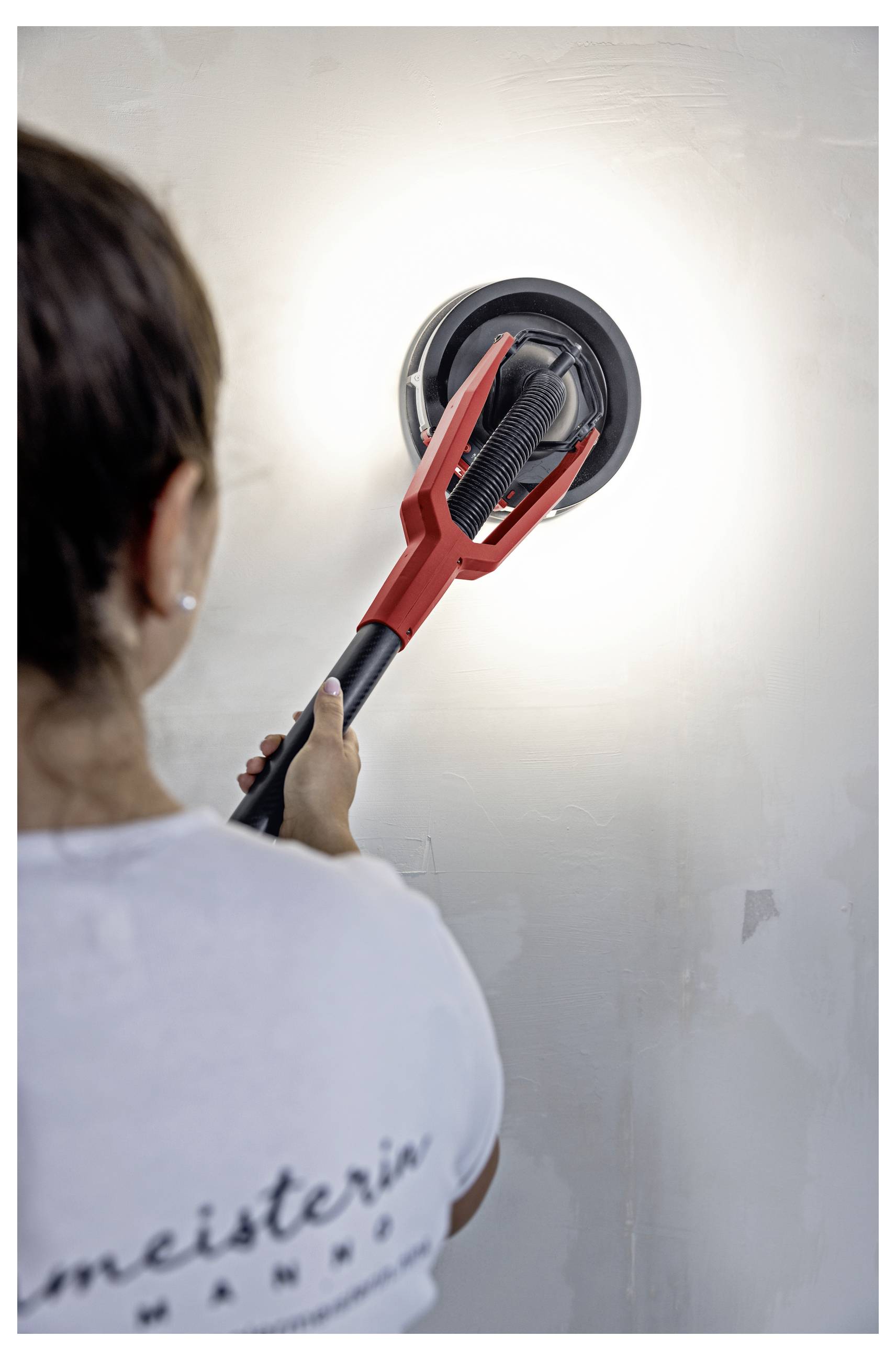 Eine Person schleift eine Wand mit einem roten Trockenbauschleifer und bereitet die Oberfläche zum Anstreichen oder Reparieren vor.