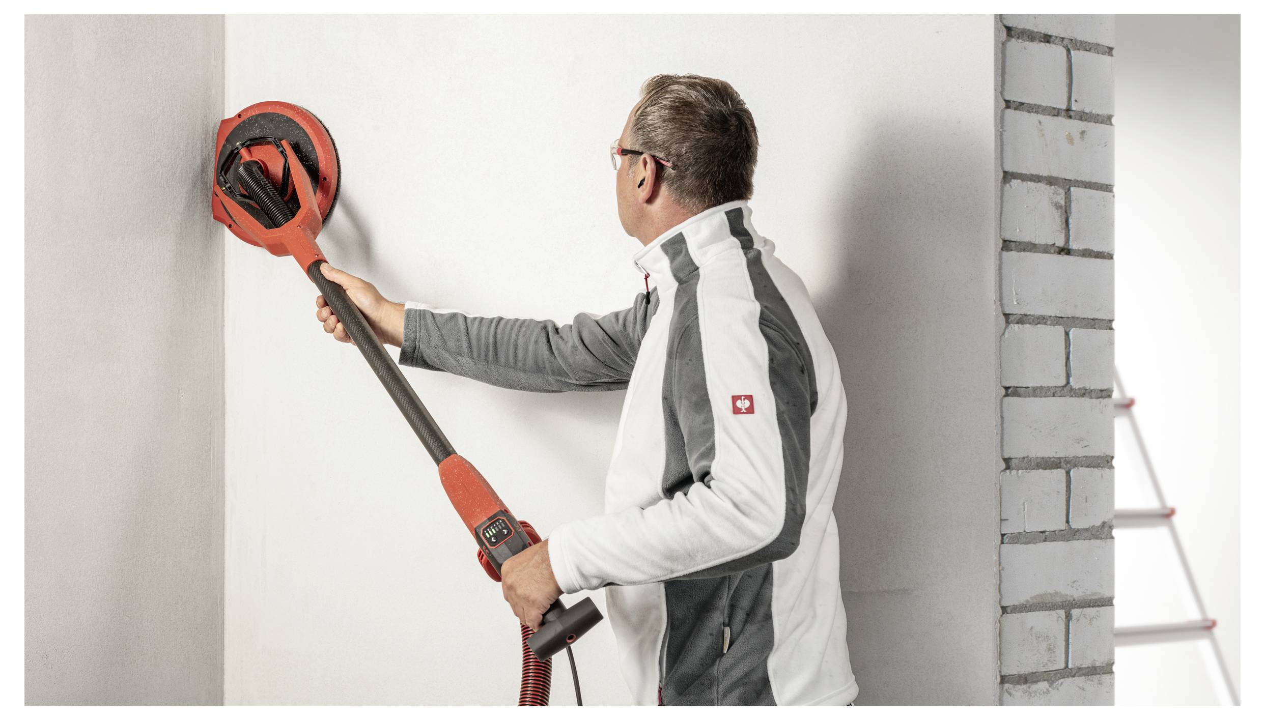 Ein Mann schleifte eine Wand mit einem tragbaren elektrischen Trockenbauschleifer während einer Innenrenovierung.