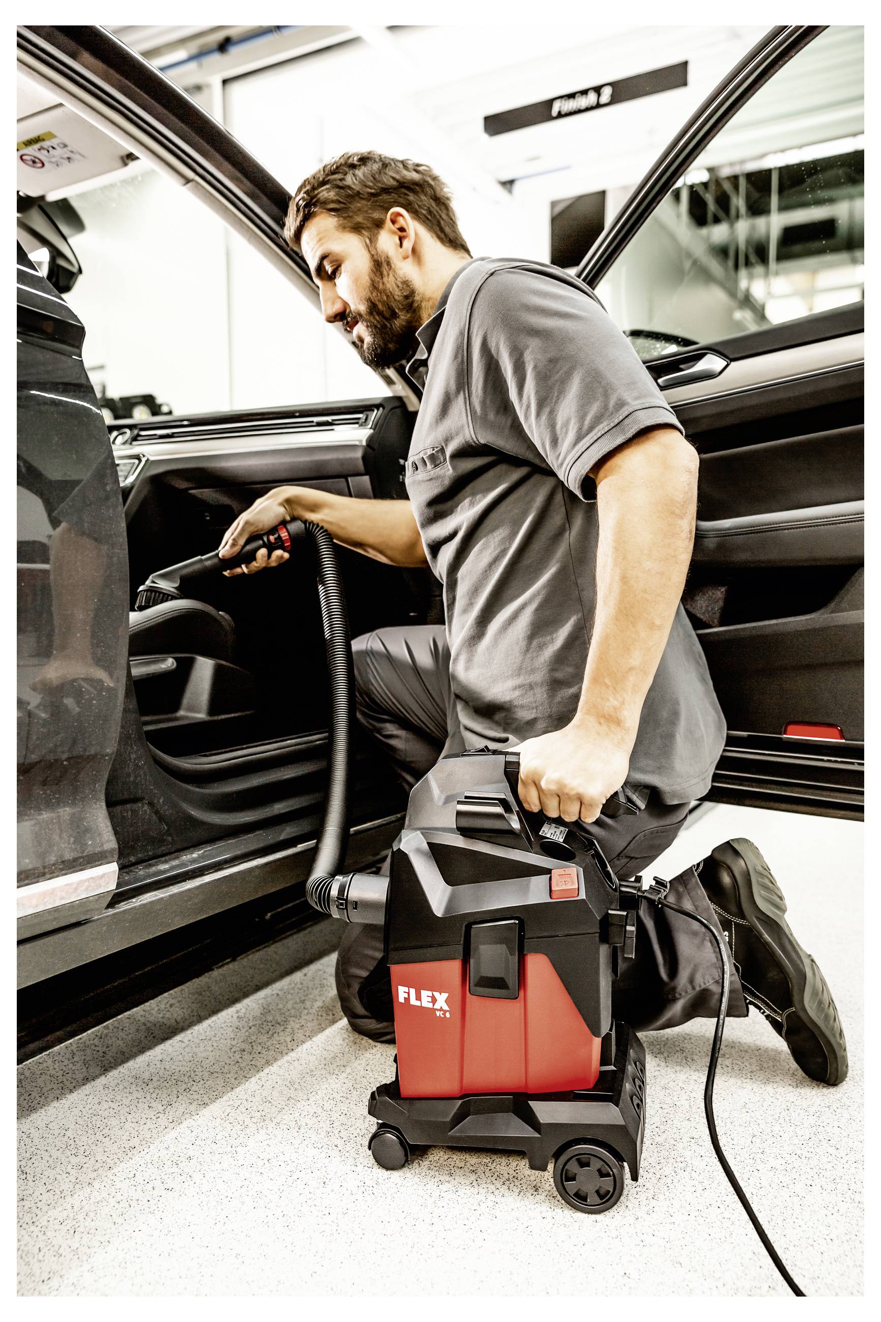 Mechaniker saugt das Innere eines offenen Autos mit einem tragbaren rot-schwarzen FLEX-Industriestaubsauger ab.