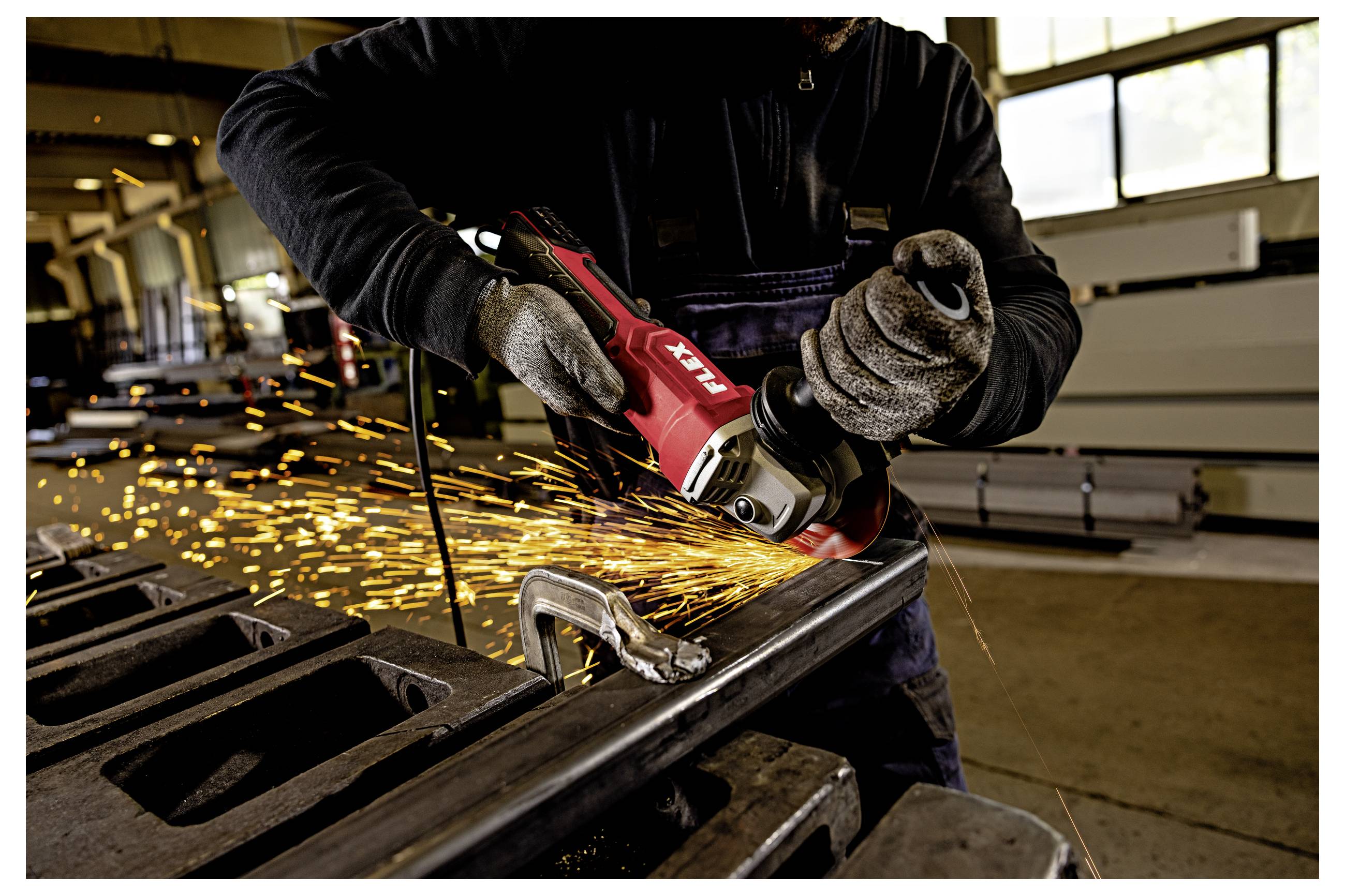 Arbeiter, der einen roten Winkelschleifers an einem Metallträger verwendet und Funken in einer Werkstatt versendet.