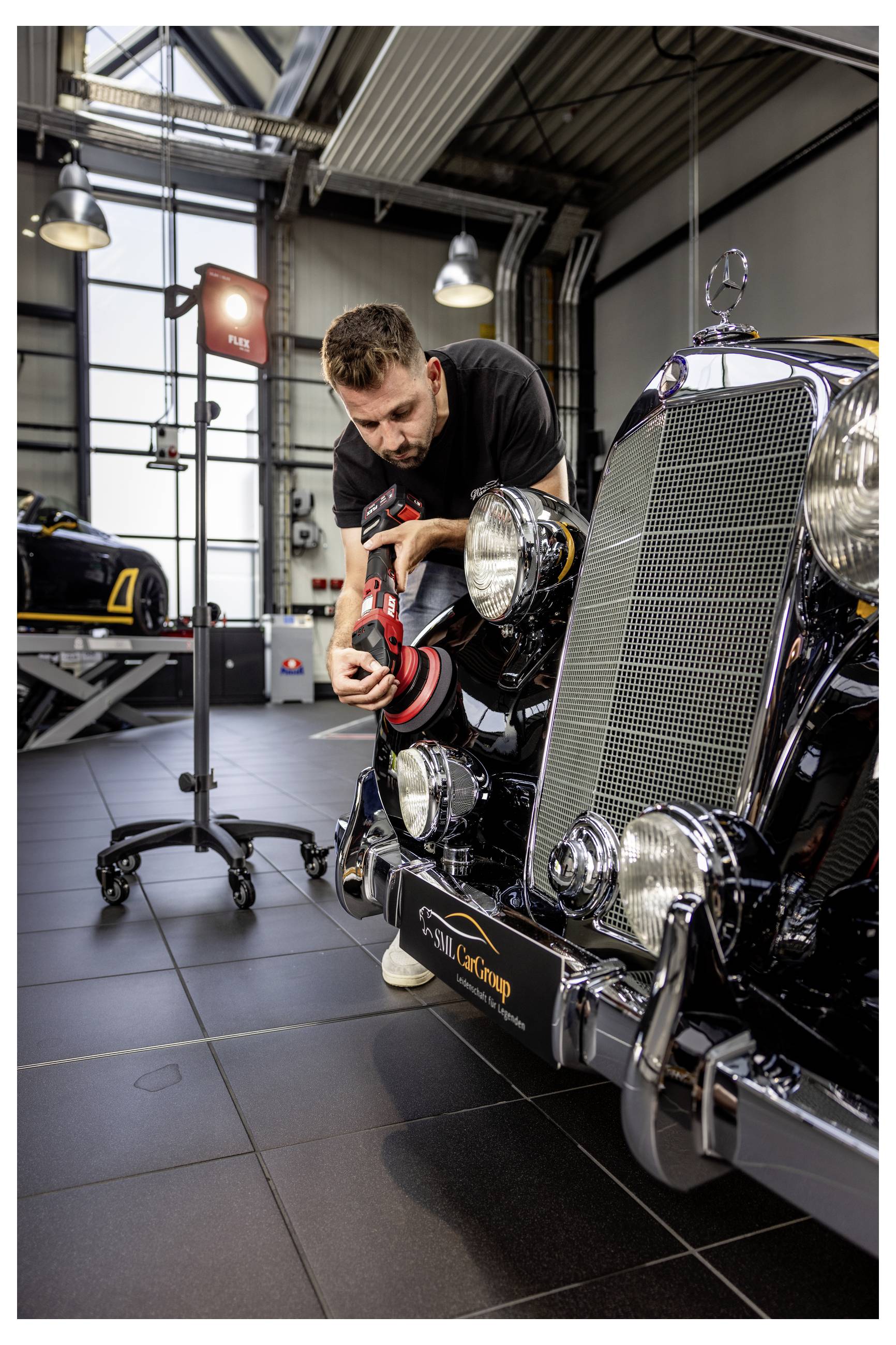 Ein Mechaniker poliert den vorderen Kühlergrill und den Scheinwerfer eines Oldtimers in einer Garagenwerkstatt.