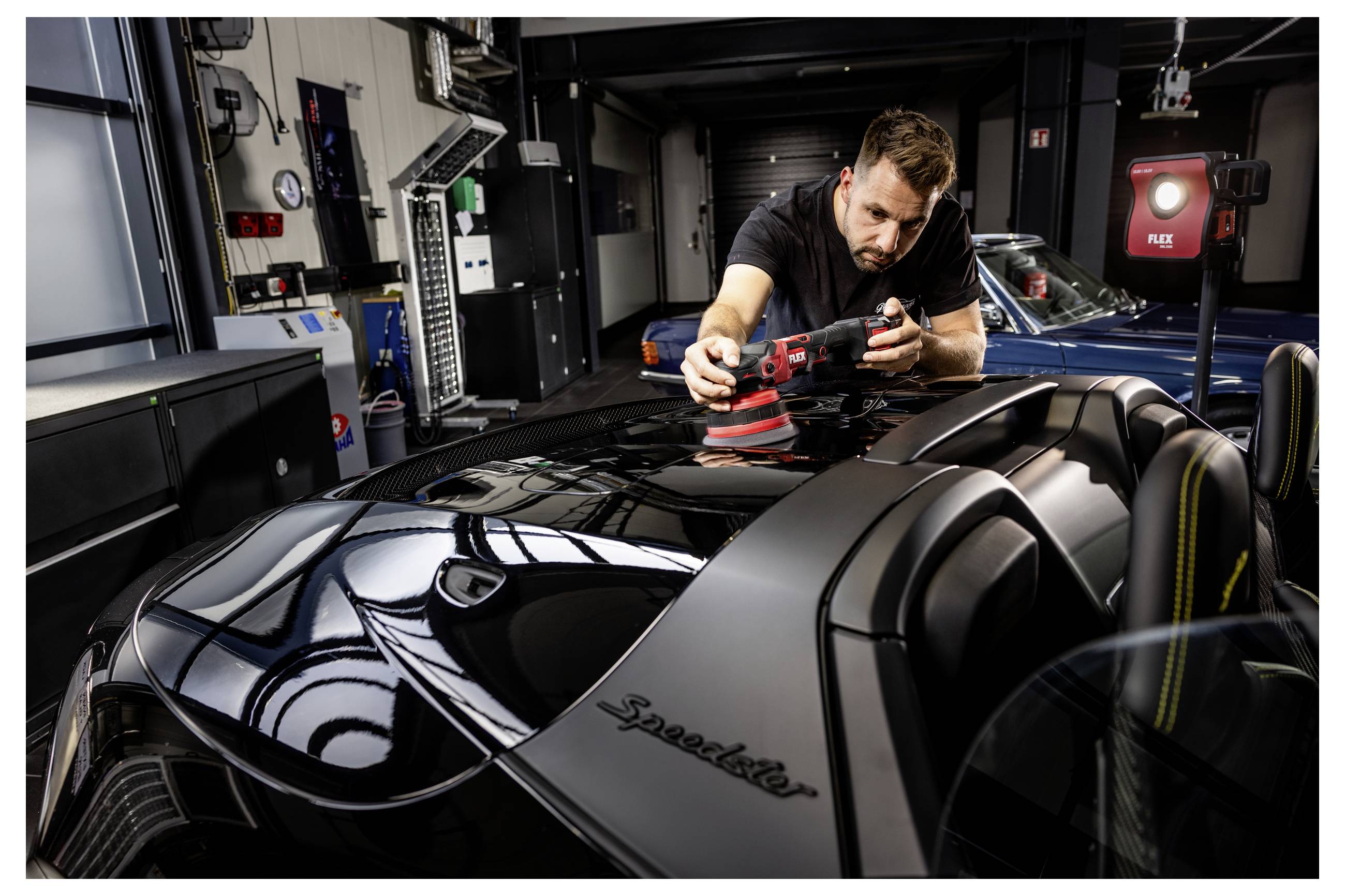 Mechaniker poliert die glänzend schwarze Motorhaube eines Performance-Fahrzeugs in einer Werkstatt mit einem Doppelhubbuffer.