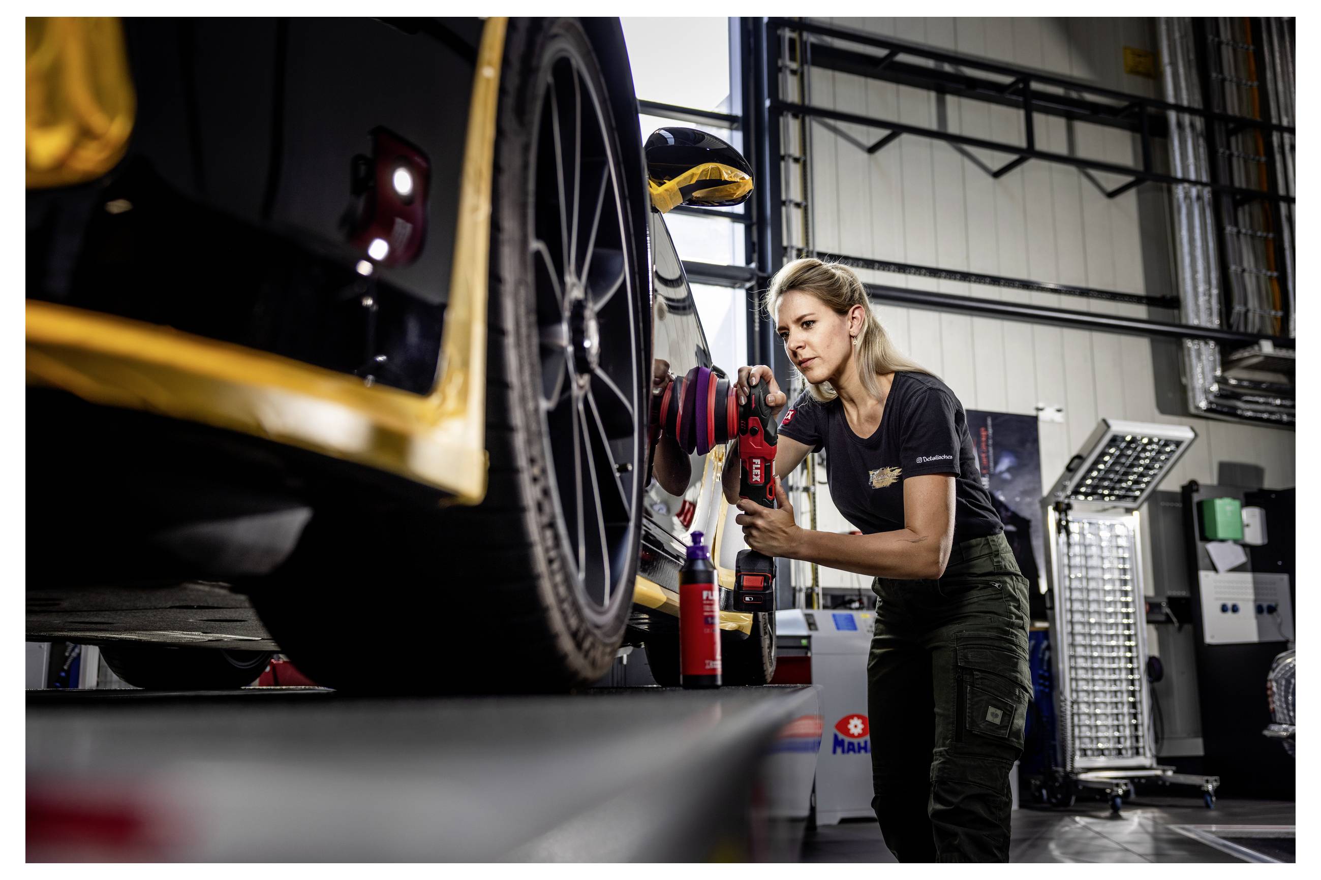 Ein Mechaniker benutzt ein Elektrowerkzeug, um das Vorderrad eines Rennwagens in einer Autowerkstatt zu warten.