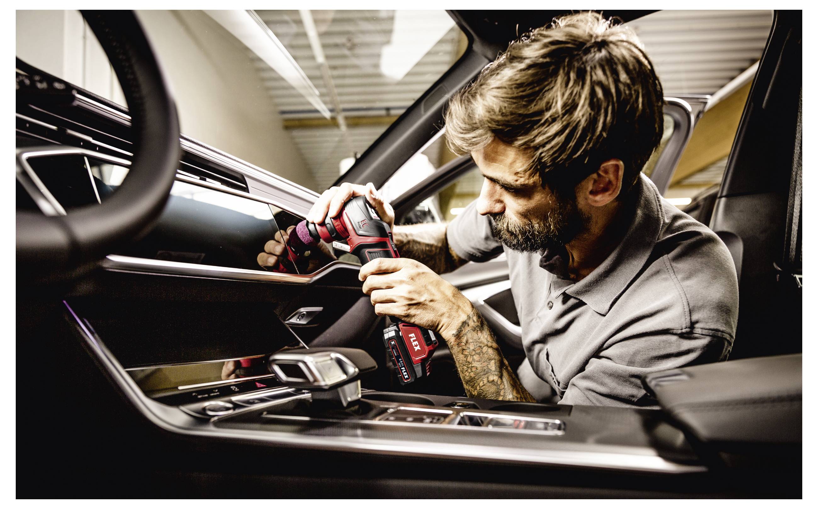 Ein Mechaniker, der einen kabellosen Bohrer verwendet, um die Innenseite einer Autotür zu installieren oder zu reparieren, während er sich in das offene Fahrzeug lehnt.