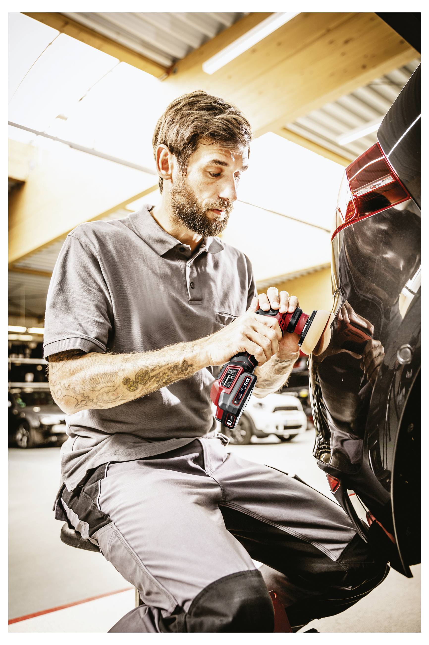 Mechaniker, der ein schnurloses Elektrowerkzeug verwendet, um an der Rückseite eines schwarzen Autos in einer Garage oder Autowerkstatt zu arbeiten.