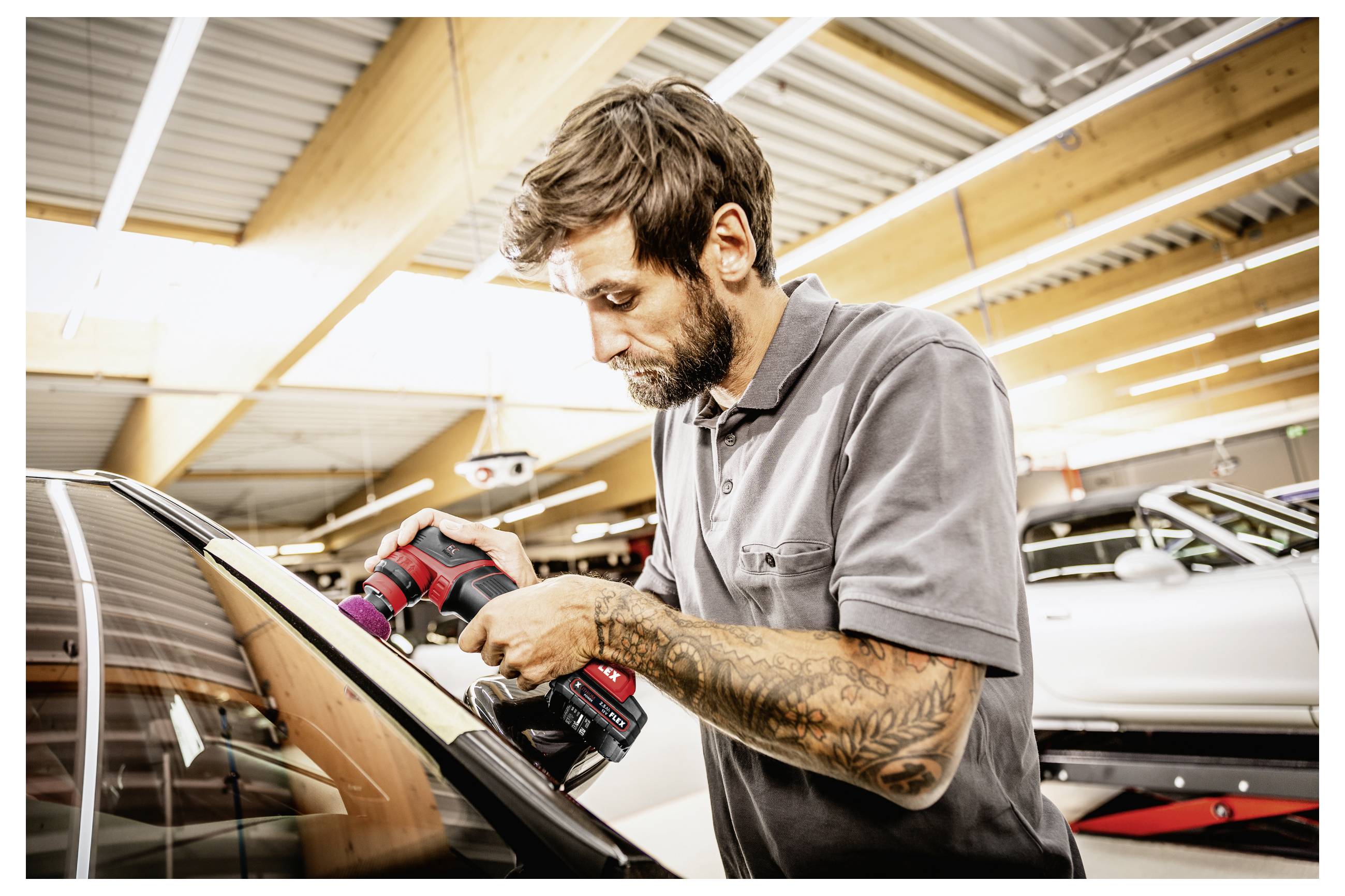 Ein Mechaniker poliert ein Autofenster mit einem kabellosen Polierer in einer Autowerkstatt.