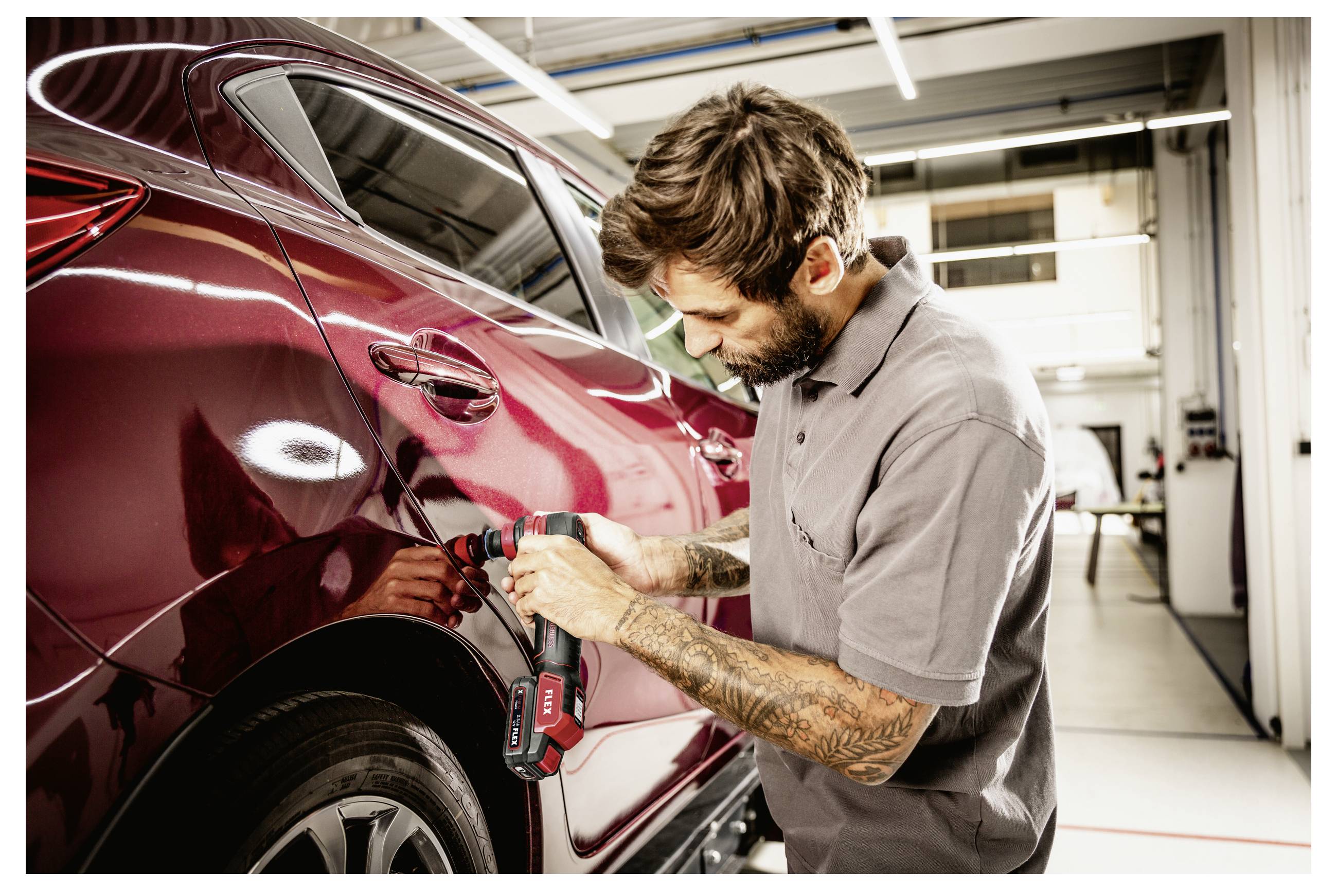 Mechaniker verwendet ein kabelloses Elektrowerkzeug, um eine Beule von einer roten Autotür in einer Karosserie-Werkstatt zu entfernen.