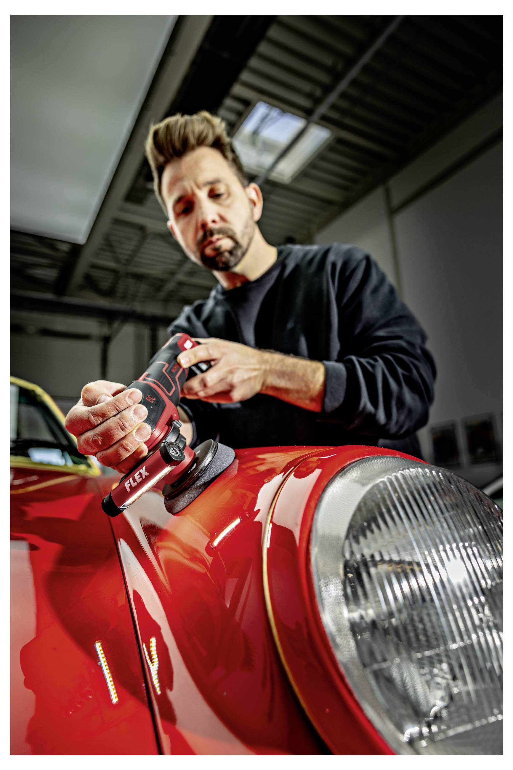 Techniker, der ein Elektroschleifsystem benutzt, um die rote Motorhaube eines klassischen Autos in einer Werkstatt zu polieren.
