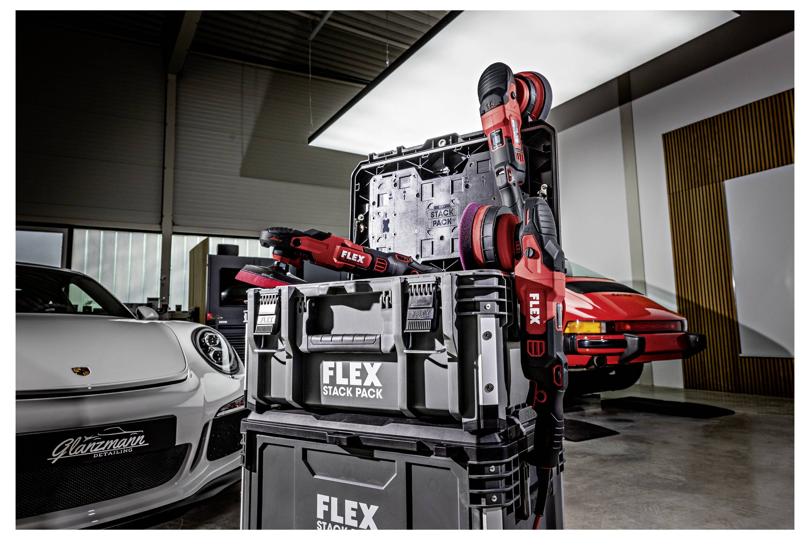 Gestapelte FLEX-Werkzeugkoffer mit roten Elektrowerkzeugen in einer Garage, mit zwei Sportwagen im Hintergrund.