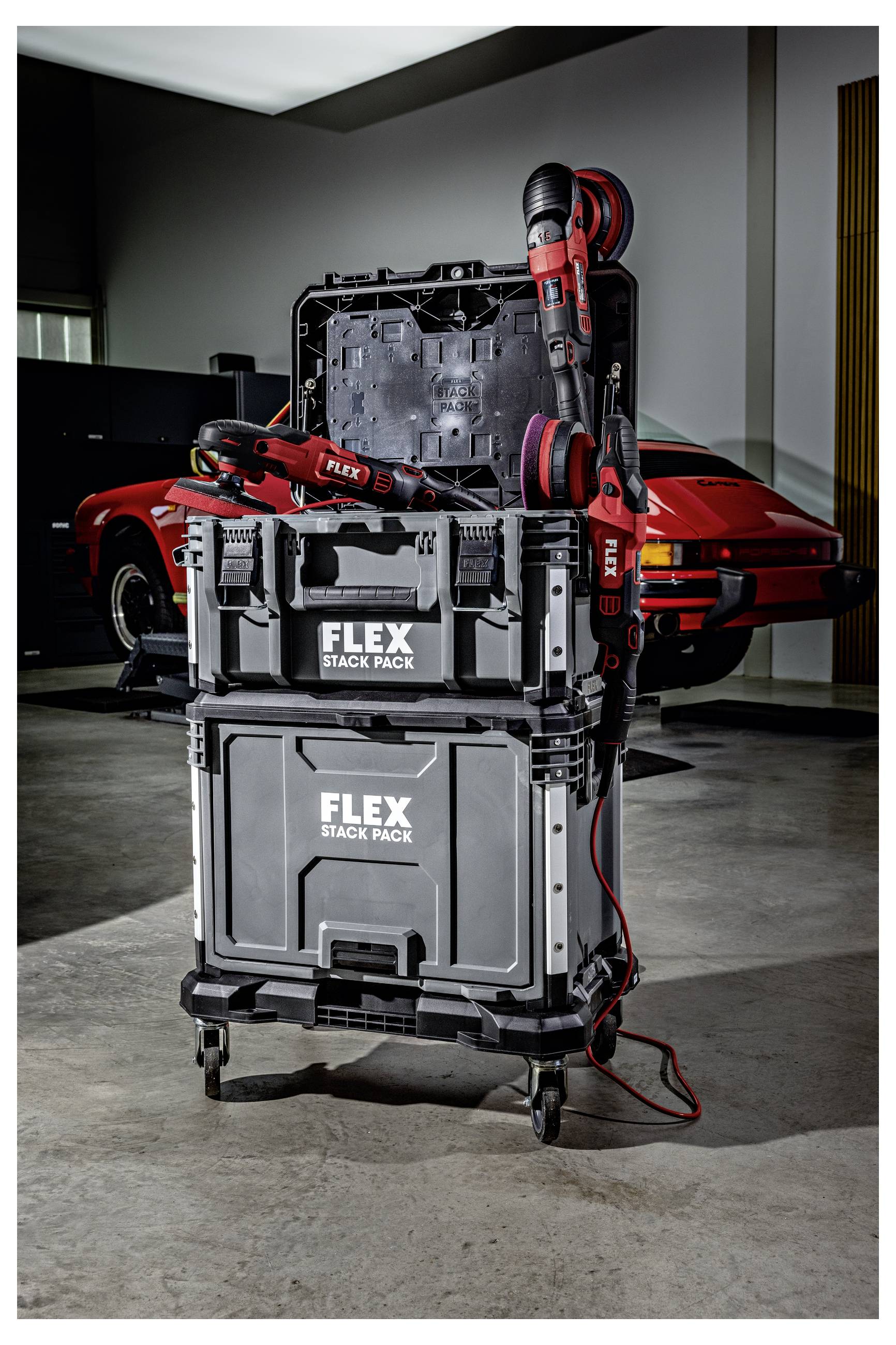 Gestapelte FLEX-Werkzeugkoffer auf einem fahrbaren Wagen mit einem roten kabellosen Elektrowerkzeug befestigt, gezeigt in einer Garage neben einem roten Sportwagen.