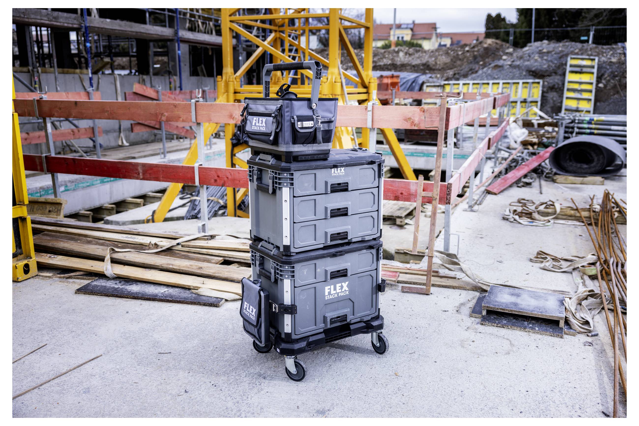 Gestapelte FLEX-Werkzeugkoffer auf einem Transportwagen auf einer Baustelle, mit Holz, Absperrungen und Ausrüstung im Hintergrund.