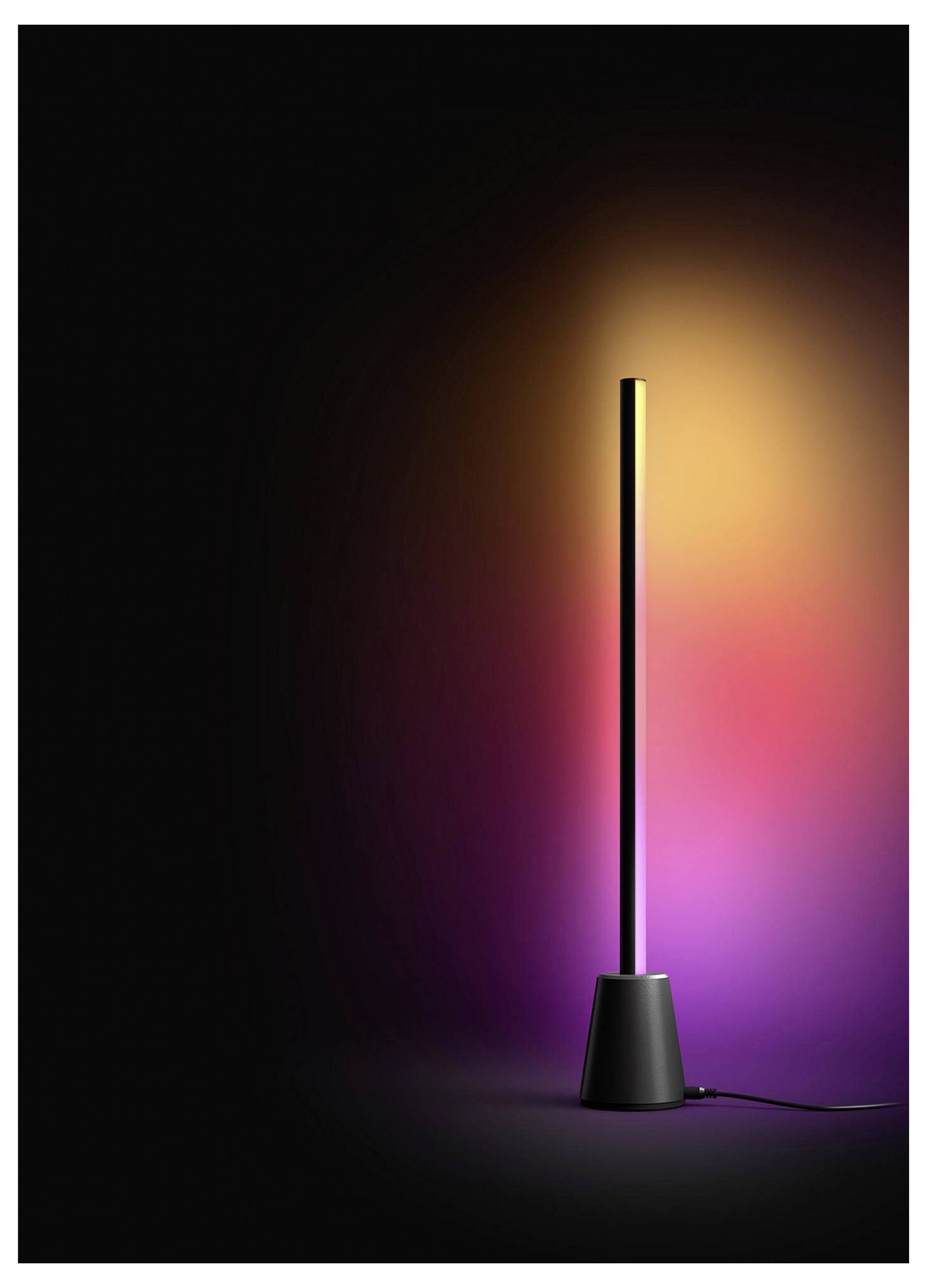 Hohe schwarze LED-Lampe auf dunklem Hintergrund, die einen warmen gelb-rosa Schimmer hinter sich wirft, mit sichtbarem Stromkabel an der Basis.