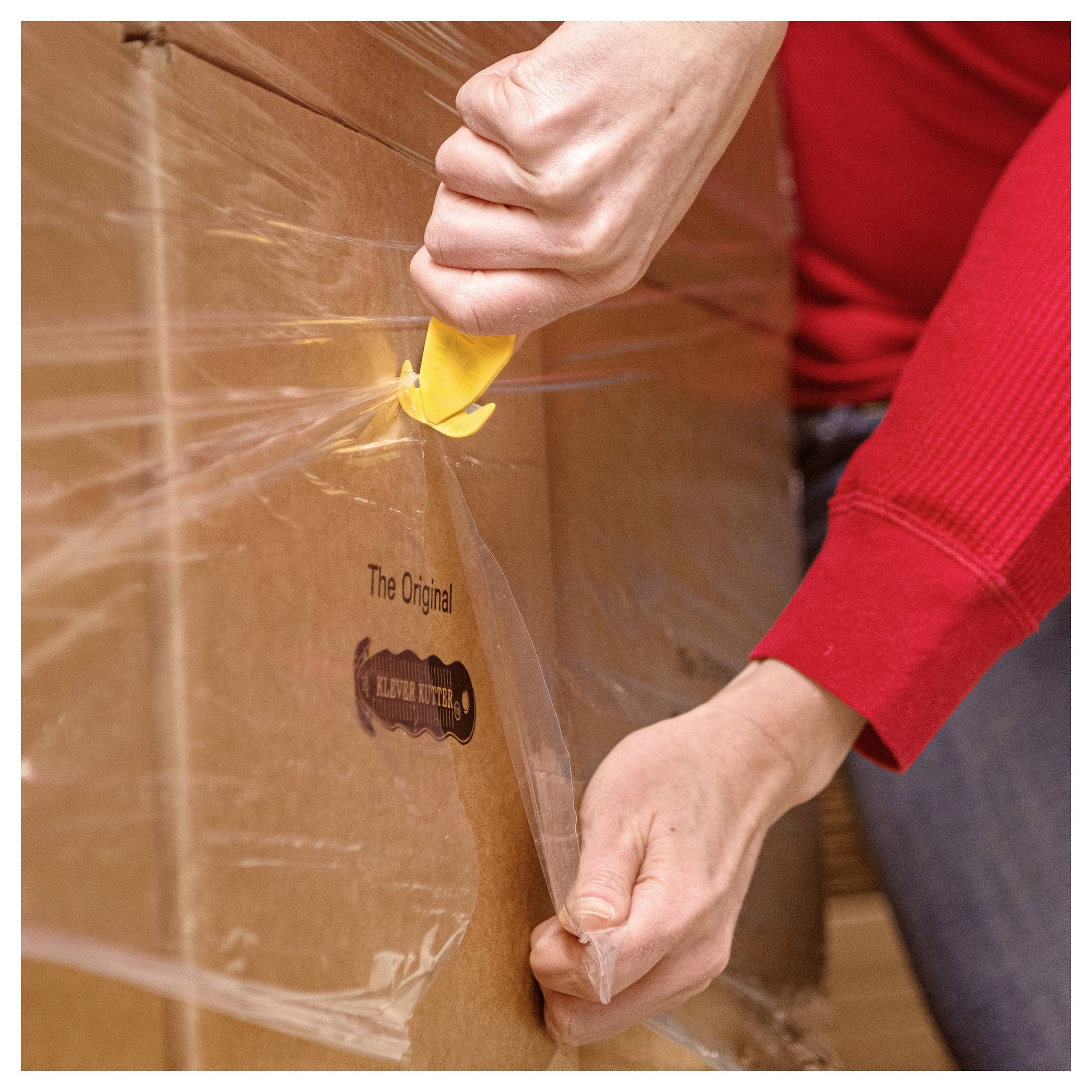 Person uses a yellow utility knife to cut open clear plastic wrap around a cardboard box.