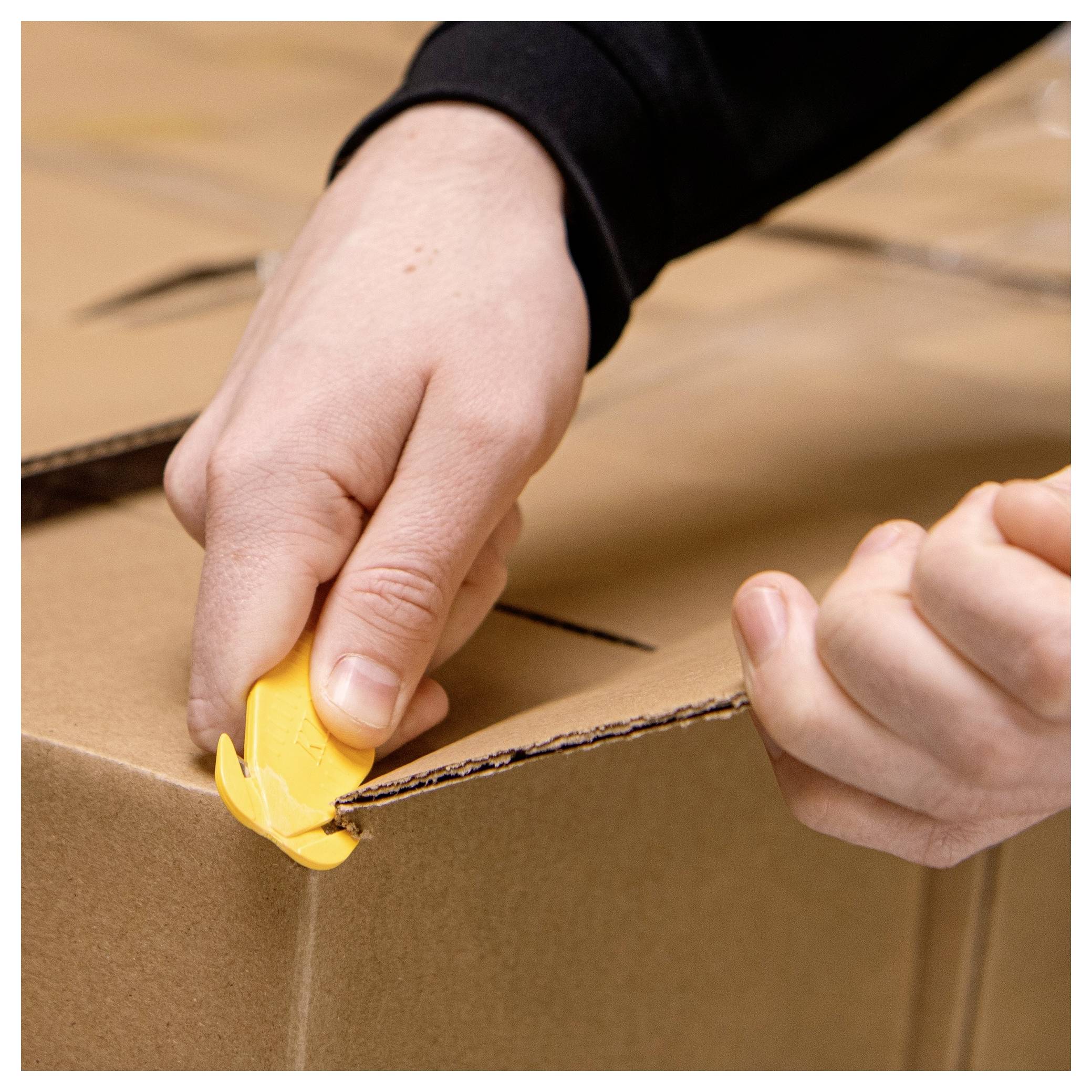Hands use a yellow box cutter to open a sealed cardboard shipping box.