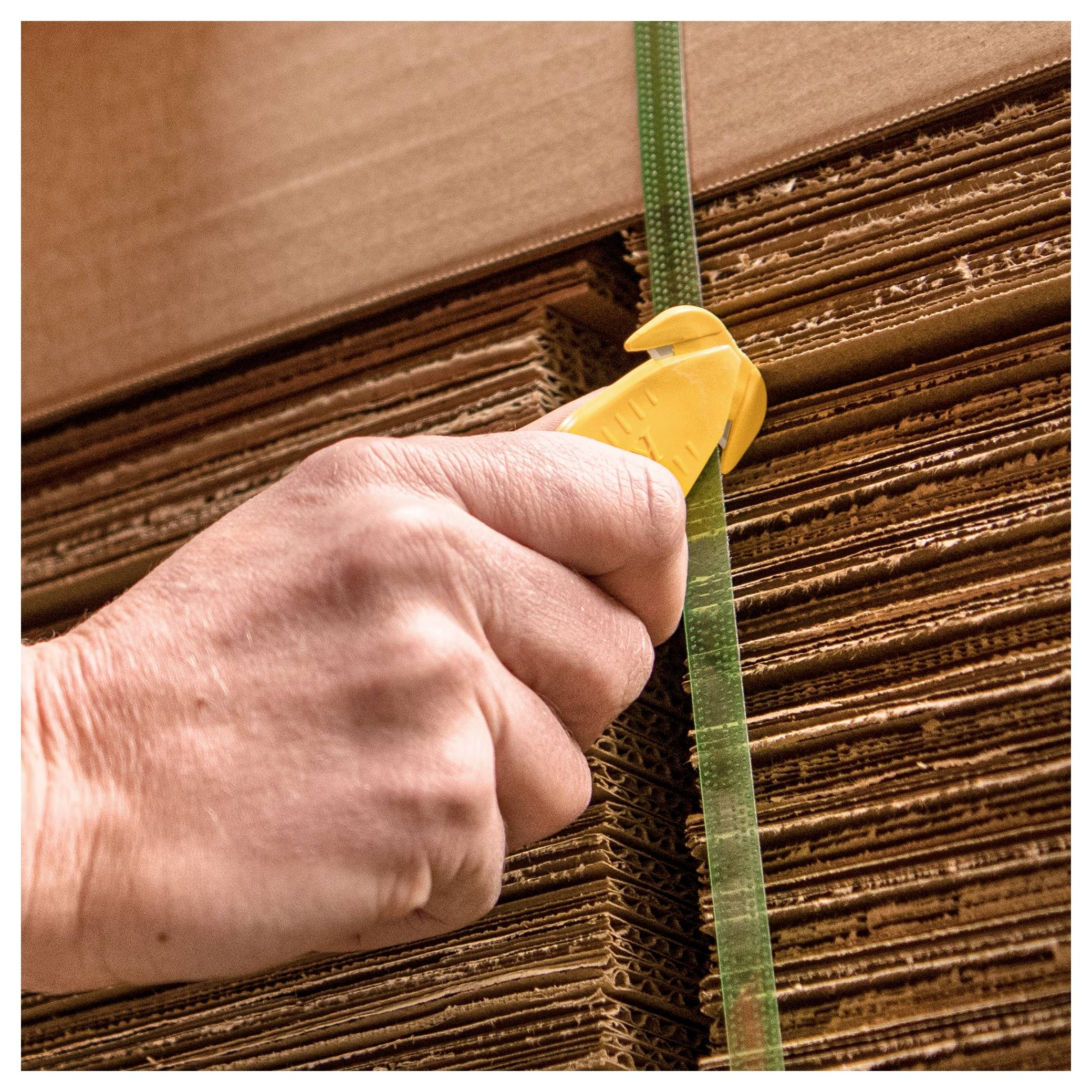 Hand tightening a green plastic strap around a stack of corrugated cardboard boxes.