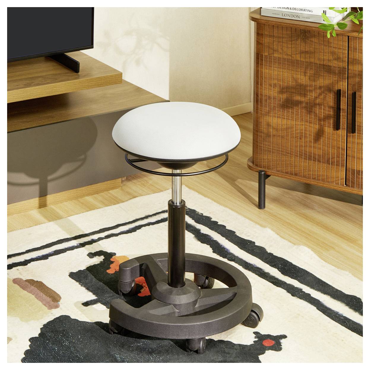 Rundhöcker mit weißem Sitz in einem modernen Wohnzimmer, neben einem Fernsehständer und einem Holzschrank auf einem gemusterten Teppich.