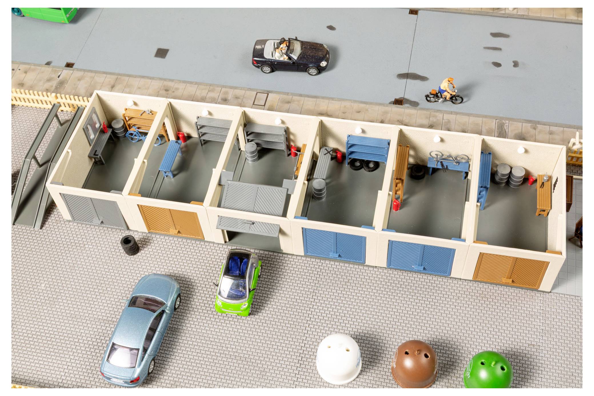 Modell einer Garage oder Werkstatt mit mehreren Räumen und Spielzeugfahrzeugen auf nahegelegenen Straßen, von oben betrachtet.