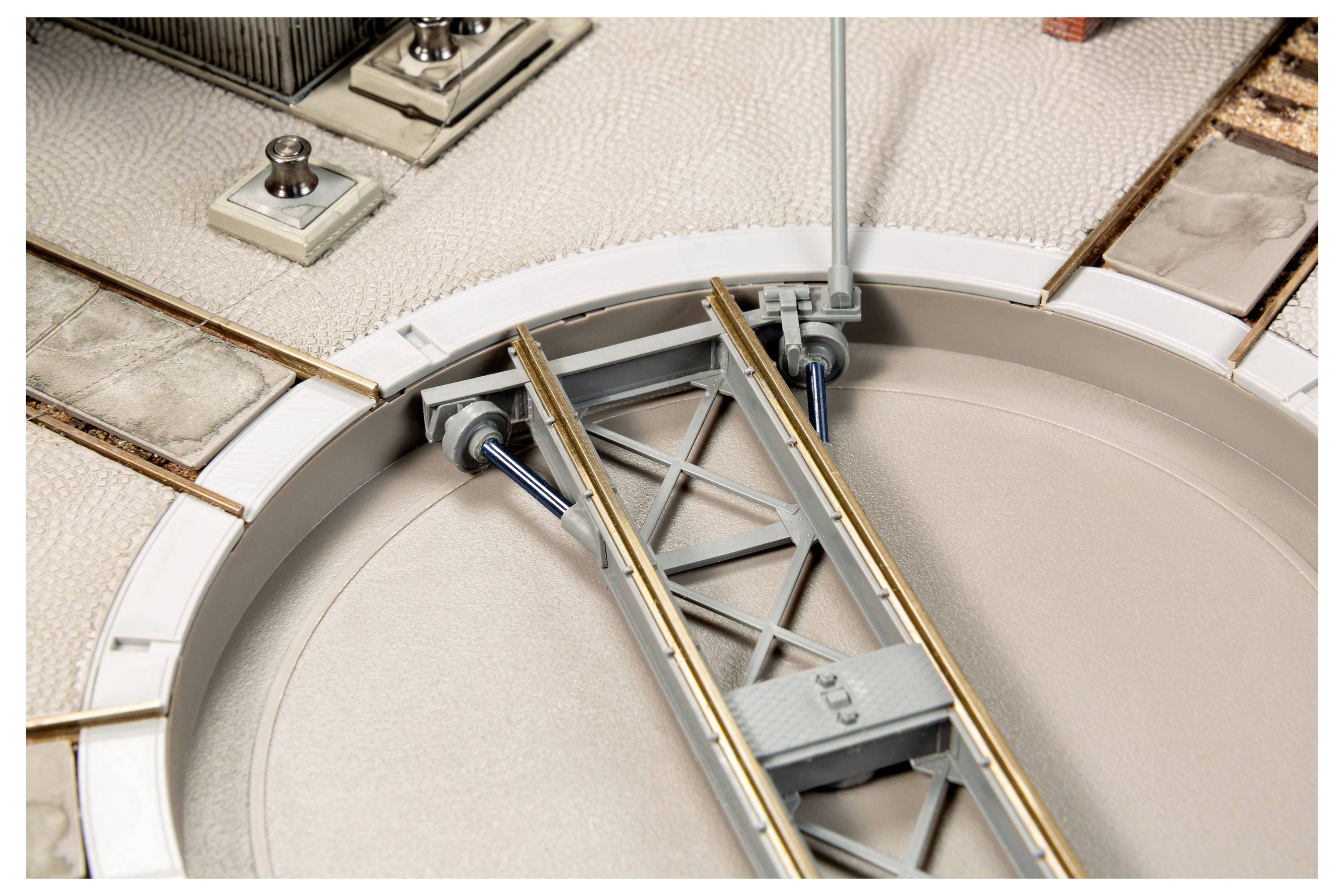 Nahaufnahme einer Modelleisenbahnschiene oder Weiche mit sich kreuzenden Metallschienen und mechanischem Gestänge in einer kreisförmigen Grube.