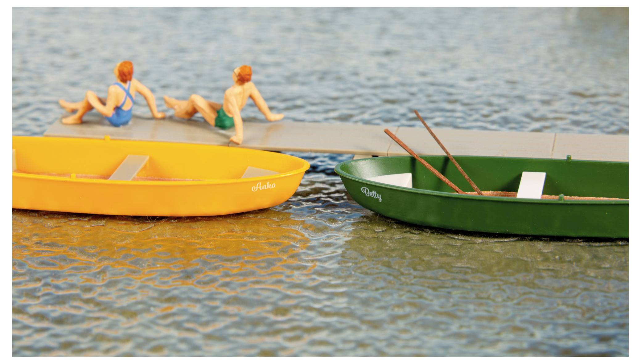 Zwei Miniaturboote schwimmen auf gewelltem Wasser, während zwei kleine rothaarige Figuren auf einem Dock neben ihnen sitzen.