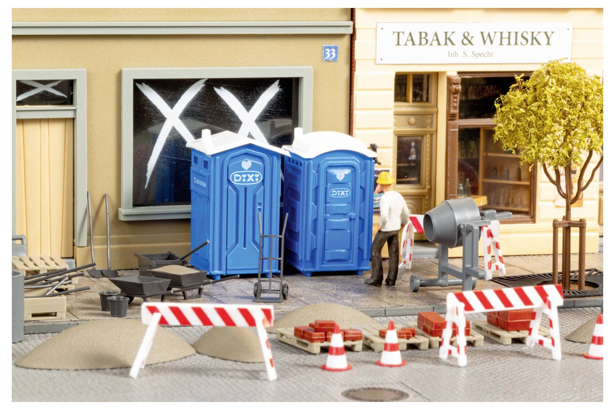Miniatur-Straßenbauszene mit zwei blauen tragbaren Toiletten, Straßenbaubarrieren, Verkehrskegeln und einem Arbeiter vor einem Geschäft mit der Aufschrift „TABAK & WHISKY