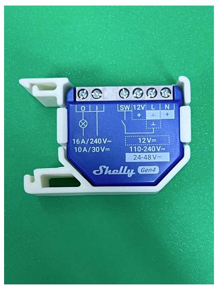 Blue Shelly Gen4 Relaismodul auf grünem Hintergrund, mit Schraubklemmen und aufgedruckten Verdrahtungsbeschriftungen für 12V und 110-240V.