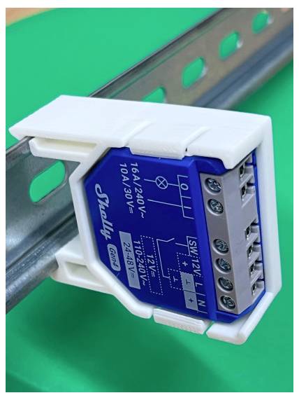 Nahaufnahme eines auf DIN-Schiene montierten elektrischen Relaismoduls mit beschrifteten Anschlüssen, blauer Blende und weißem Kunststoffgehäuse.