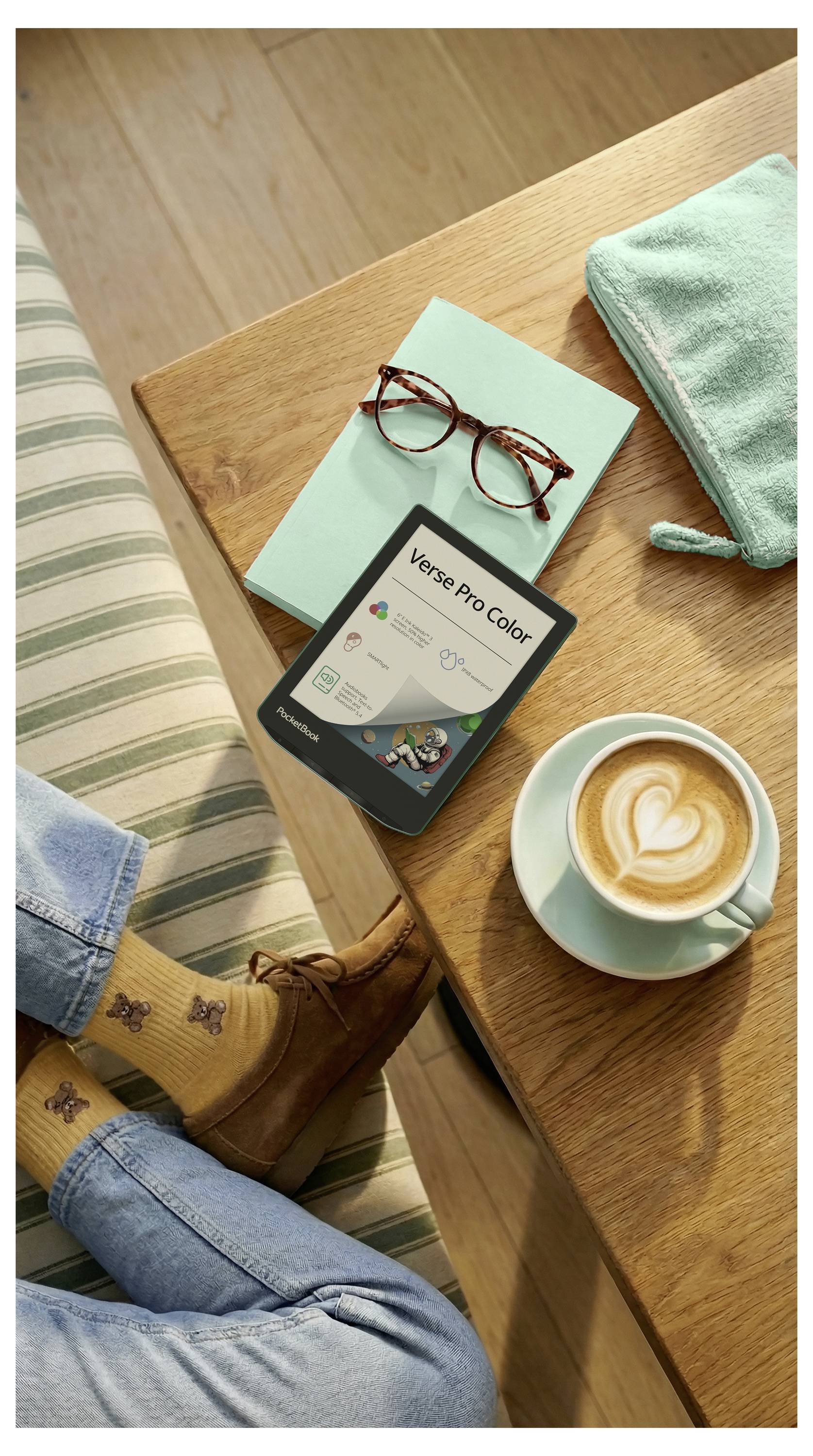 Vogelperspektive einer Person, die sich an einem Holztisch entspannt, mit einem Telefon, einer Brille, einem Kaffee, einem gefalteten Handtuch und Stiefeln, was eine gemütliche Morgenauszeit andeutet.