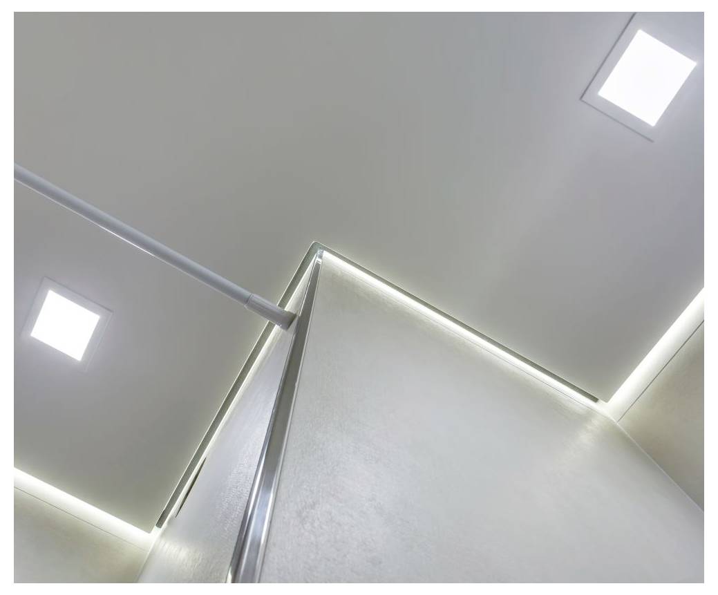 Blick auf eine hellgraue Deckenecke mit eingelassenen quadratischen Leuchten und LED-Streifenbeleuchtung entlang der Kanten.