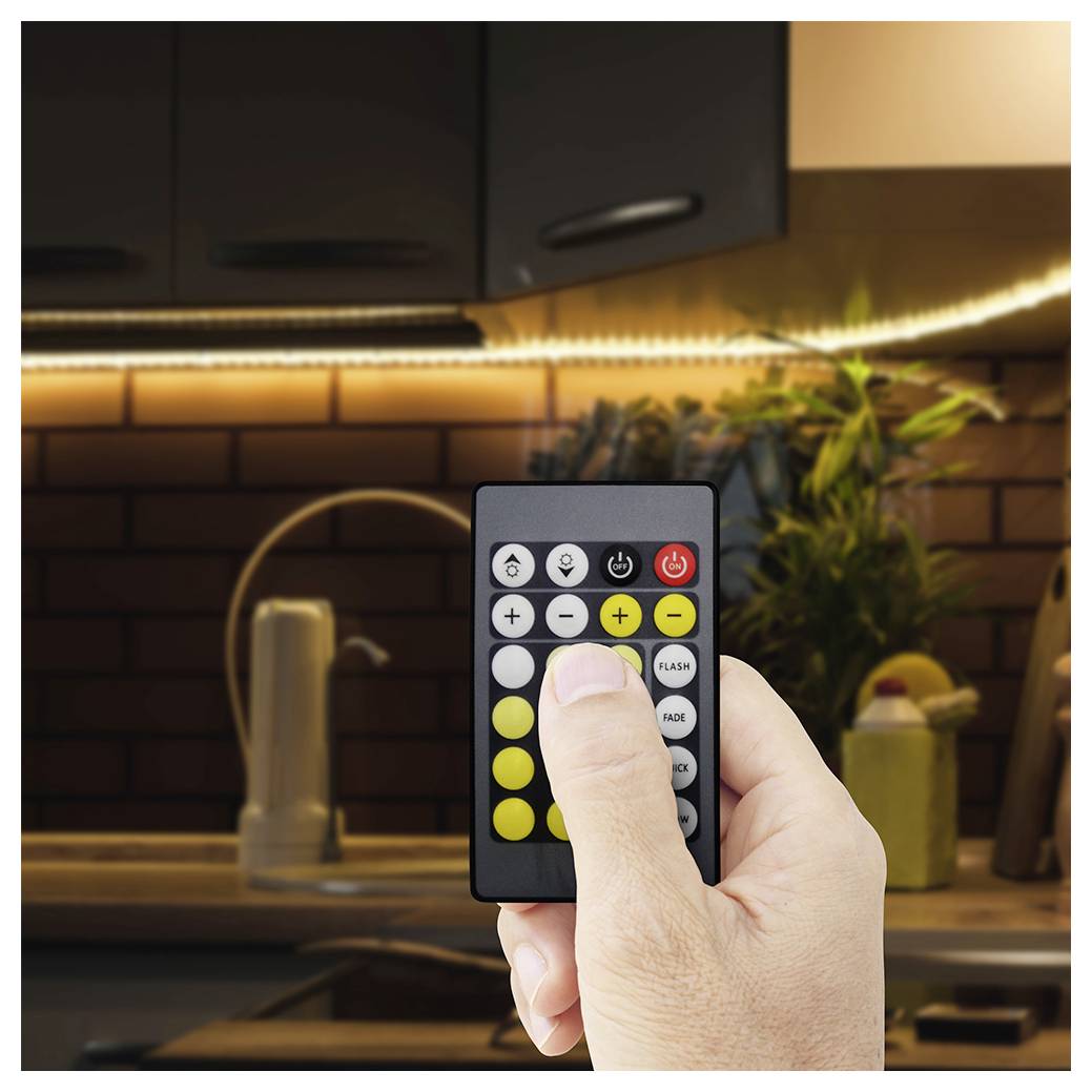 Eine Hand, die eine Fernbedienung hält und auf einen LED-Lichtstreifen in einer Küche abzielt, wobei der Finger einen Knopf drückt, um die Lichtfarbe oder Helligkeit zu ändern.