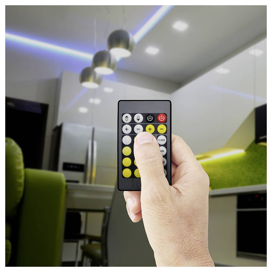 Hand hält eine Fernbedienung, die auf eine Deckenleuchte gerichtet ist, mit sichtbaren farbigen Lichtleisten in einer modernen Küche.