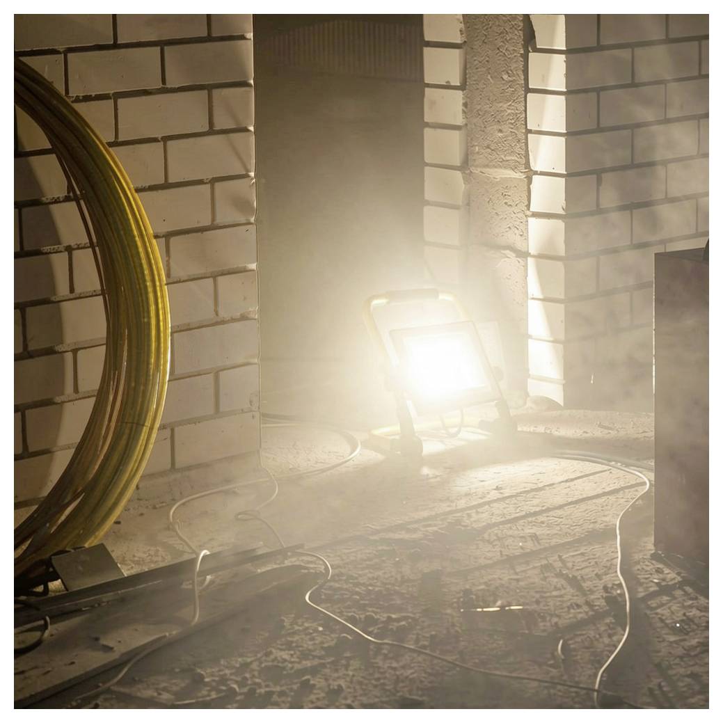 Helles Arbeitslicht auf dem Boden beleuchtet einen staubigen Baustellenbereich mit Ziegelwänden und aufgewickeltem Kabel.