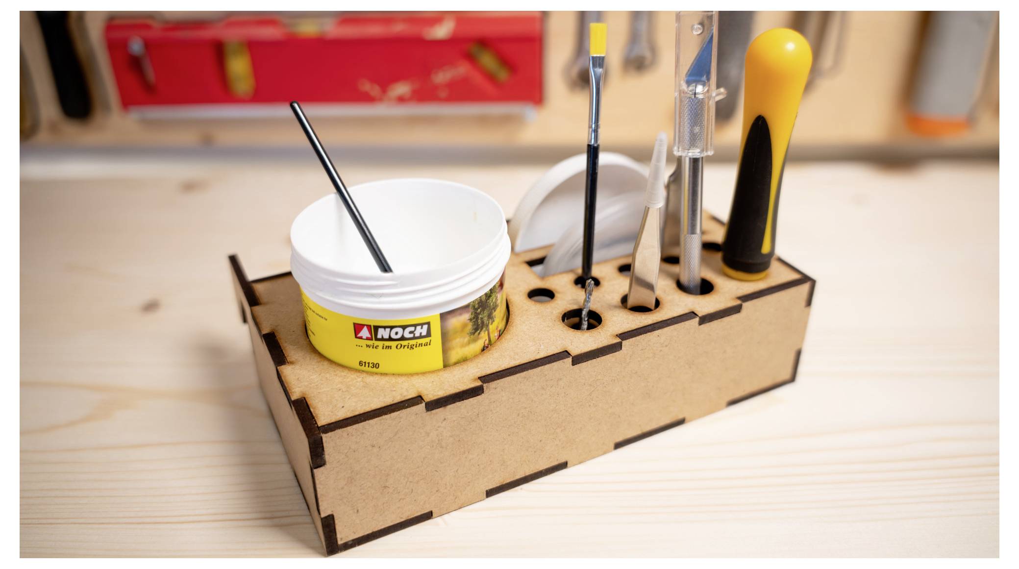 Holzschreibtischorganizer mit Pinseln, Hobby-Werkzeugen und einem kleinen Farbbehälter auf einer Werkbank.
