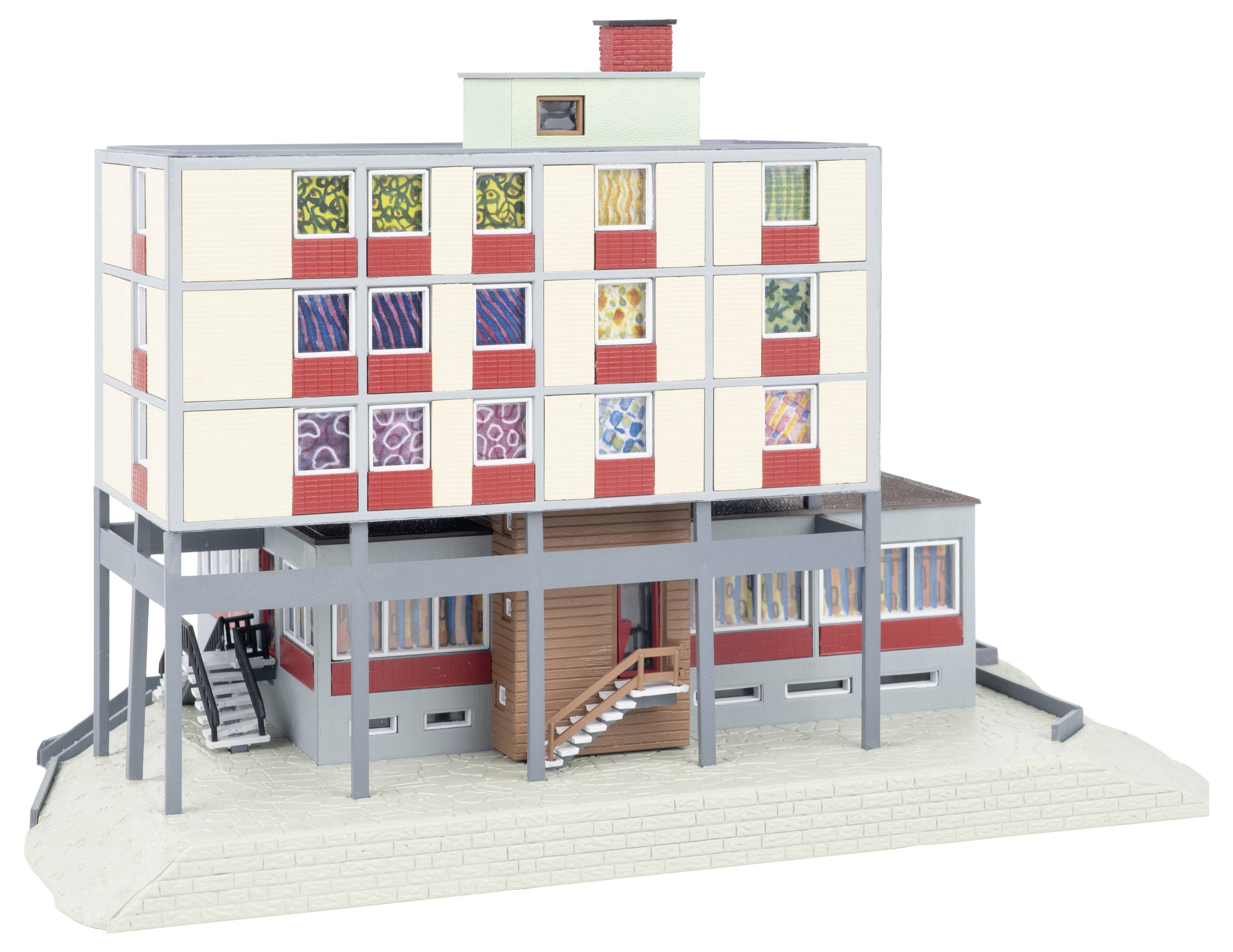 Architekturmodell eines mehrstöckigen modernistischen Gebäudes auf Stelzen, mit farbenfrohen gemusterten Fenstern, außenliegenden Treppen und einem erhöhten Obergeschoss über einem unteren Eingangsbereich.