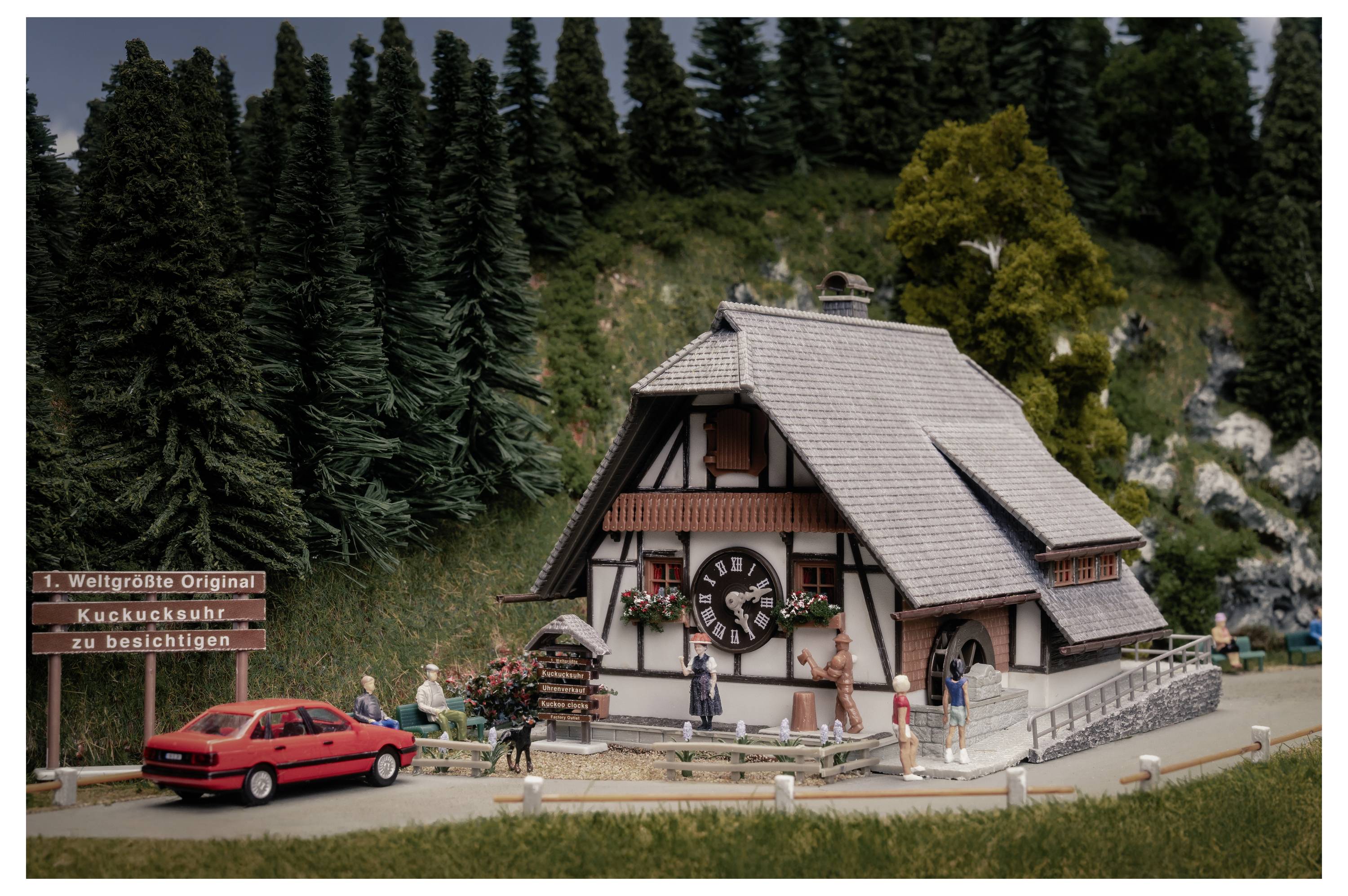 Attraktion eines miniaturisierten Berghauses mit Besuchern, einem roten Auto und einem Schild mit der Aufschrift „Weltgrößte Original Kuckucksuhr zu besichtigen