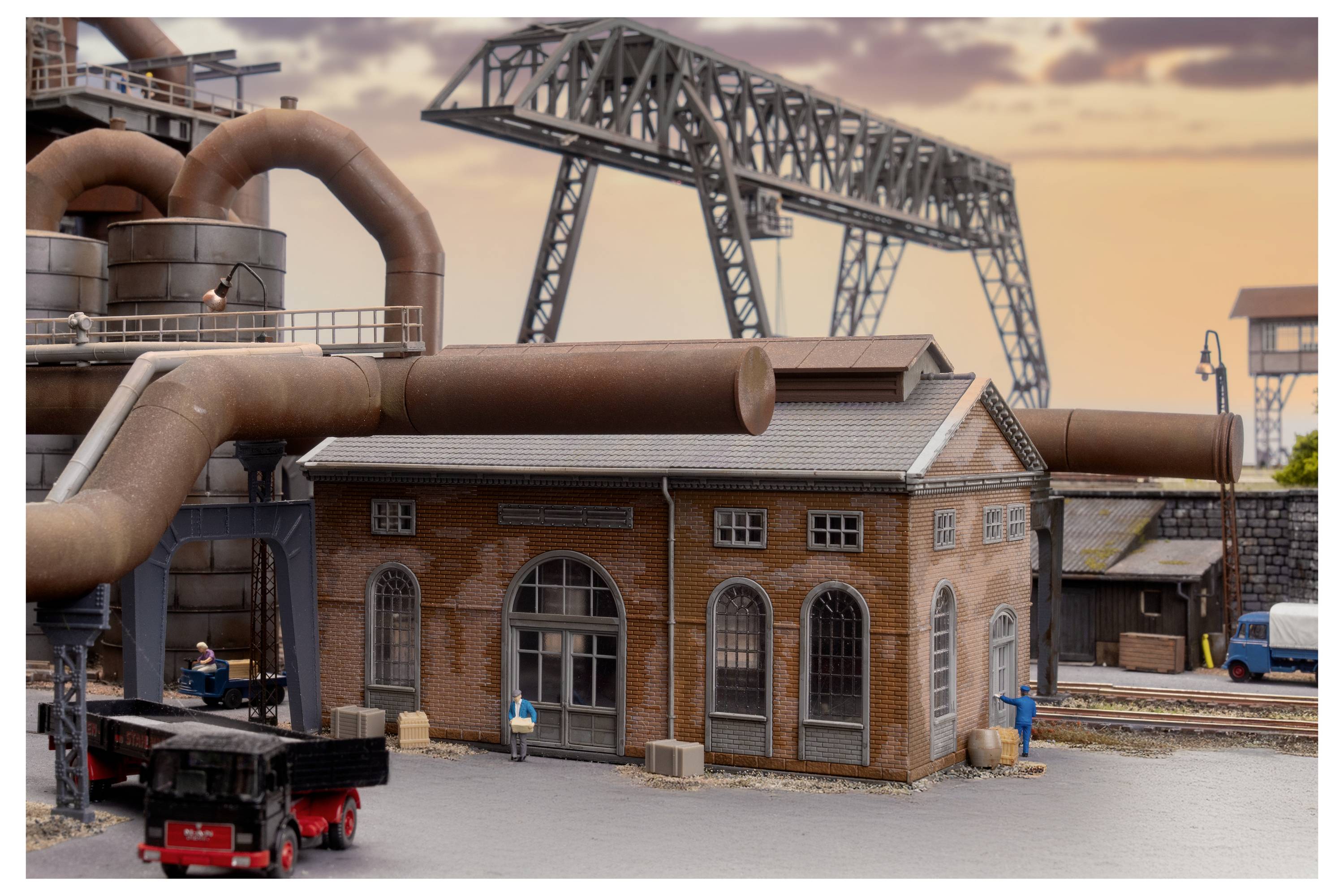 Modelliertes Industrieszenario mit einem Ziegelfabrikgebäude, großen rostfarbenen Rohren und Stahlkonstruktionen für Überkopfförderanlagen bei Sonnenuntergang.