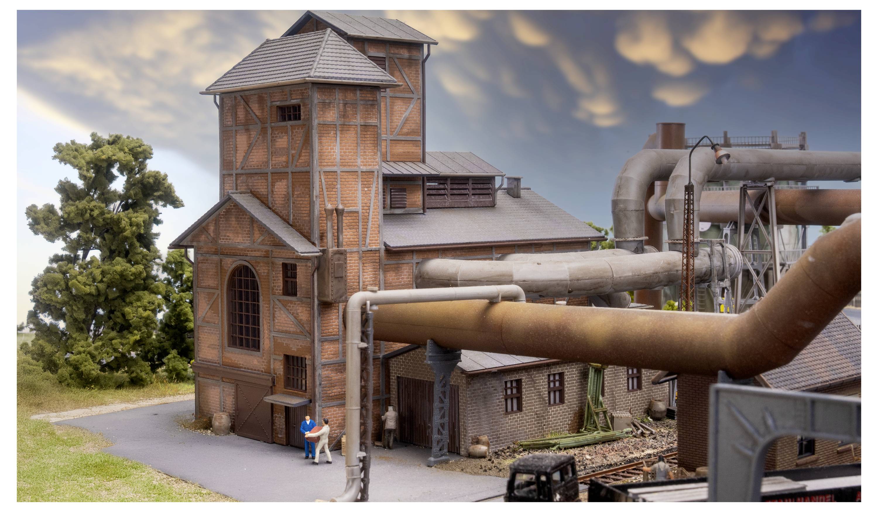 Ein detailliertes Industrieanlagenmodell mit rostigen Rohren, Backsteinttürmen und kleinen Figuren neben dem Gebäude.