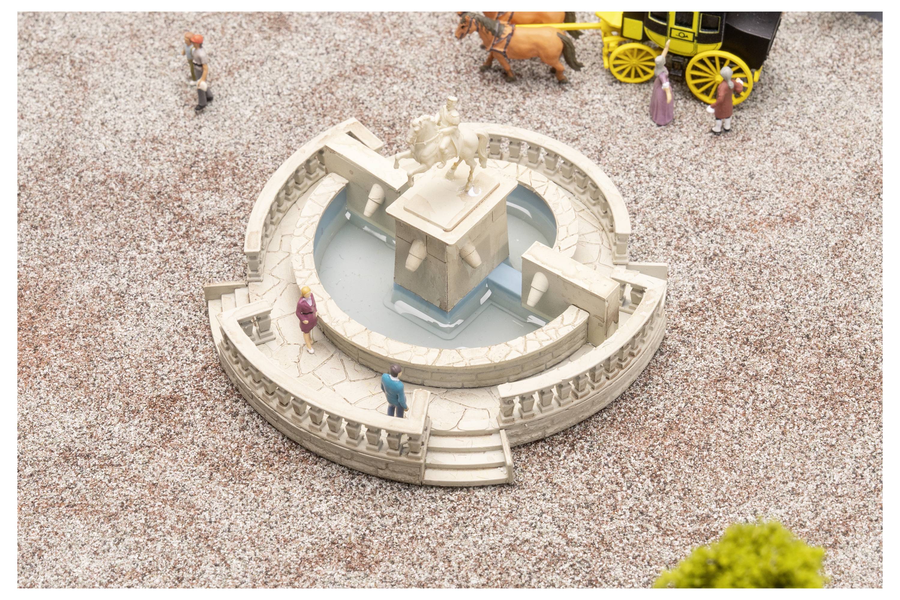 Winziger Steinbrunnen mit Pferdestatue auf einem kleinen Platz, umgeben von kleine Figuren und einer Pferdekutsche