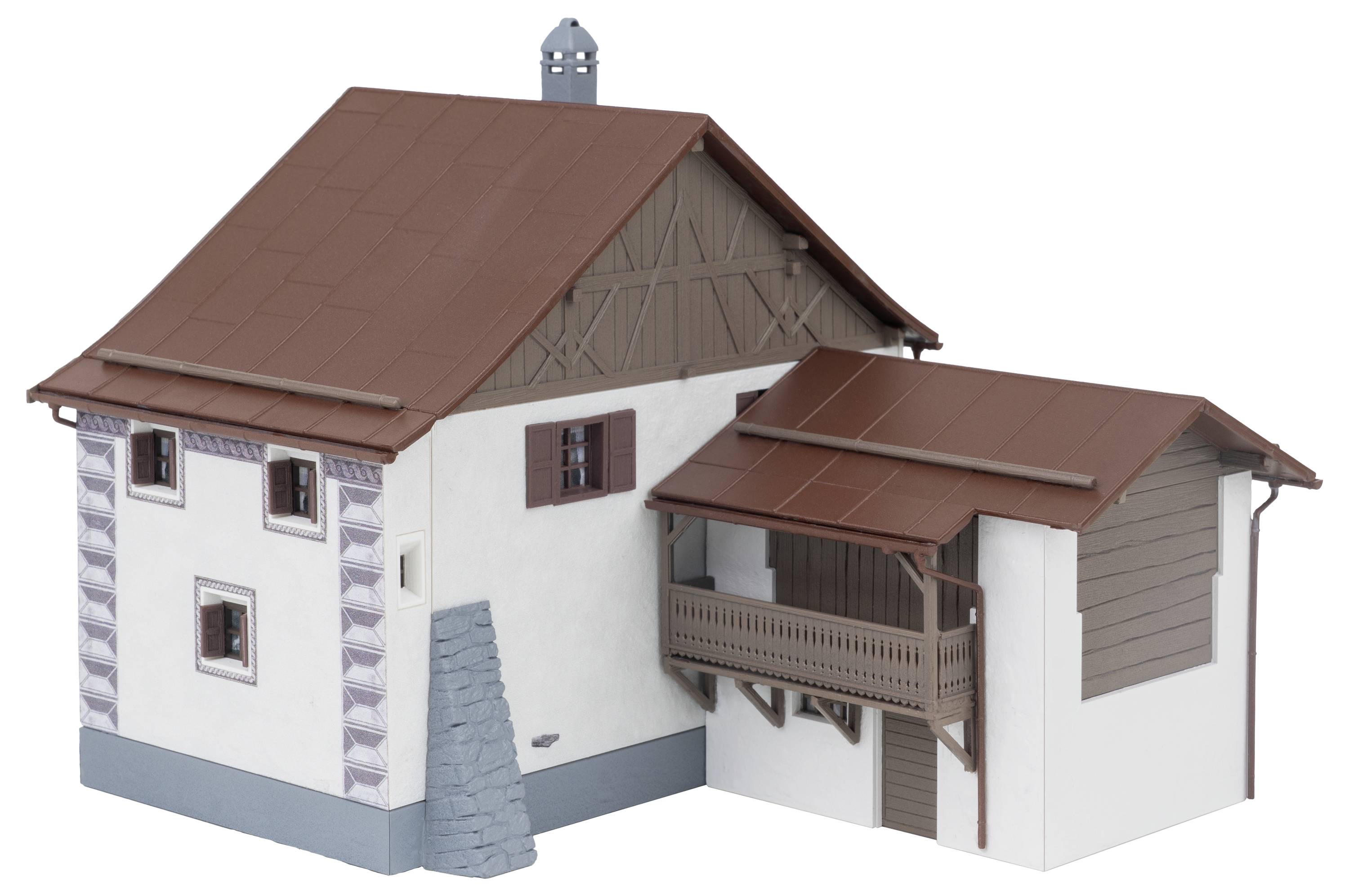 Kleines Modell eines weißen Hauses mit rotem Dach, braunem Holzgiebel und Seitenbalkon, das an eine garagenähnliche Erweiterung angebaut ist.