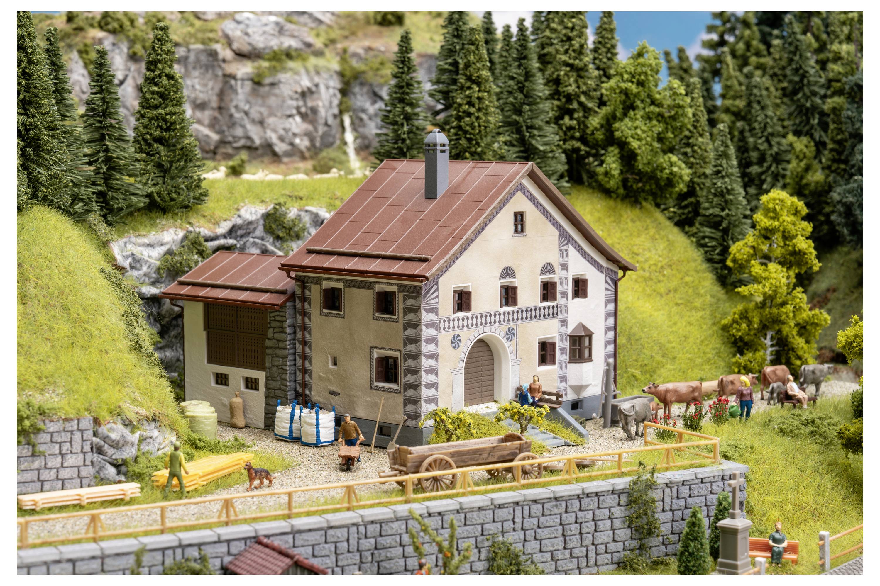 Miniaturmodell eines ländlichen Hauses mit rotem Dach auf einem Hügel, mit Menschen, Bänken und weidenden Kühen in einer gestalteten Dorfszene.